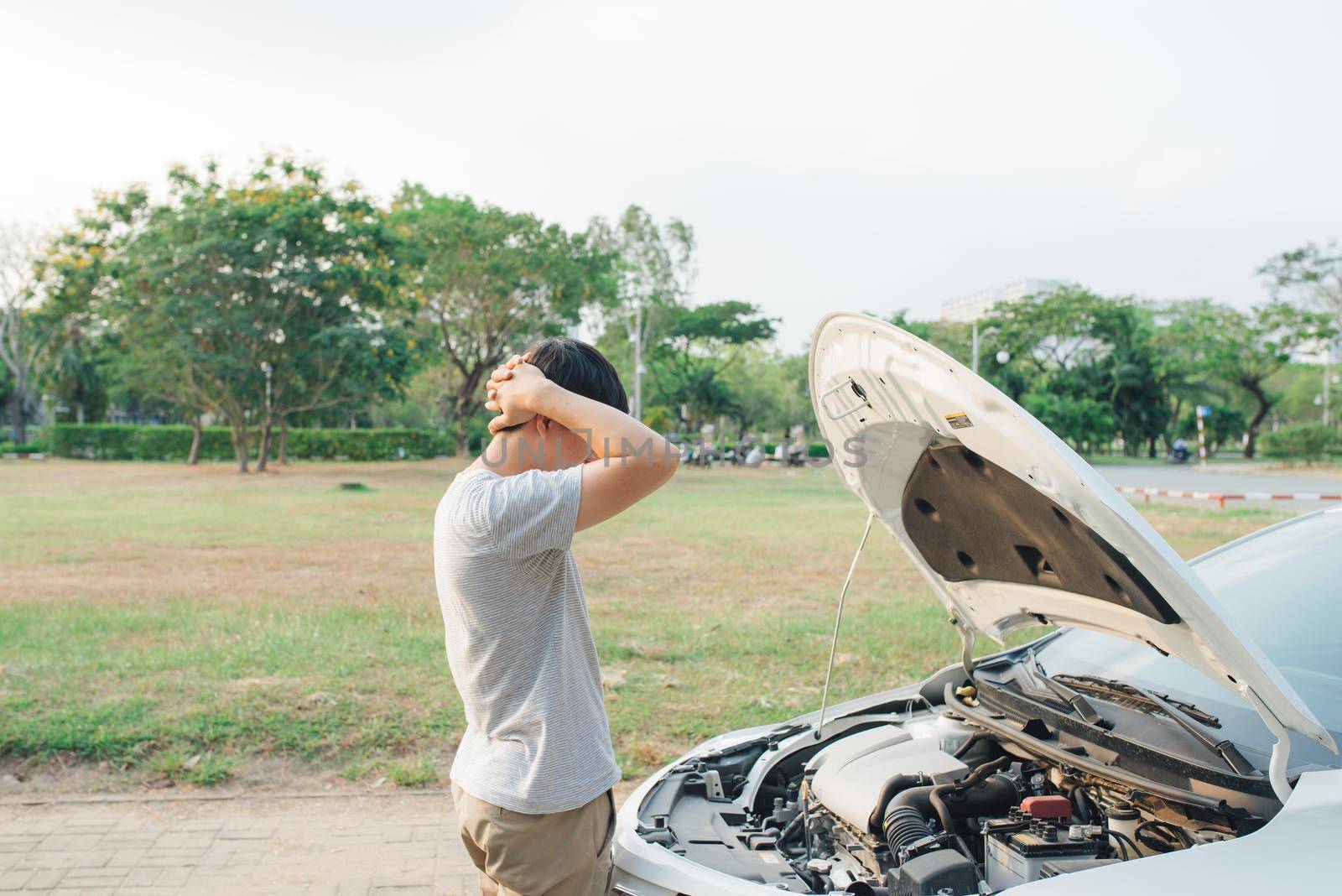 young stressed man having trouble with his broken car looking in frustration at failed engine