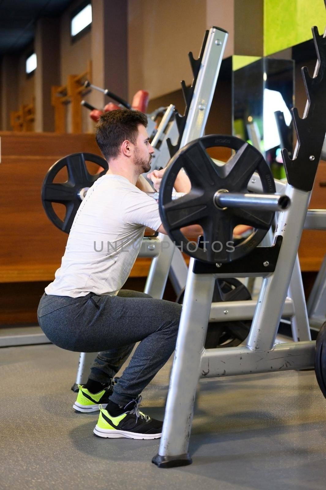 Fit man Squats With Barbell Back In Front Of Mirror Inside Gym. High quality photo.