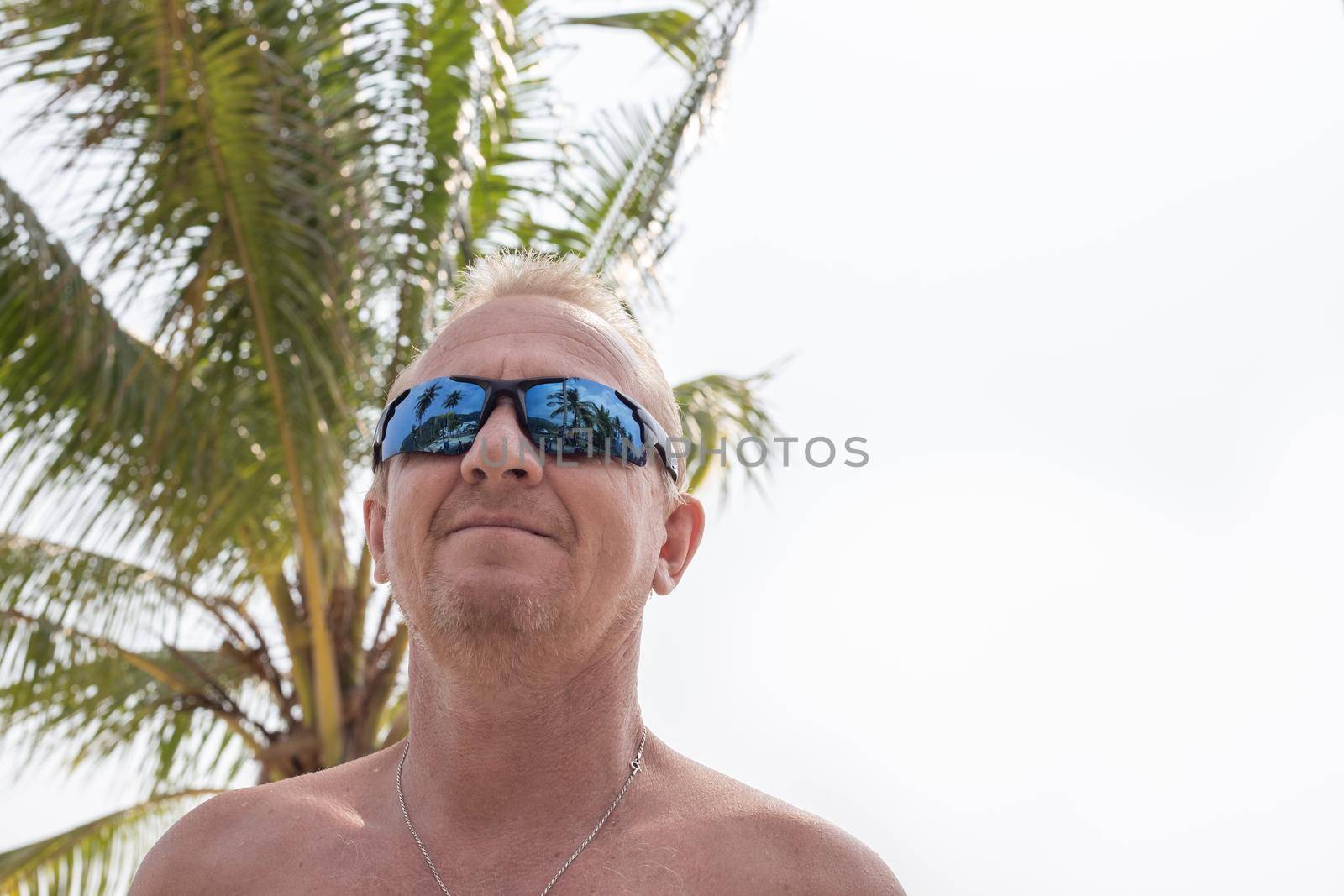 Blond man with a naked torso on the background of a palm tree, copy space. Travel and tourism.