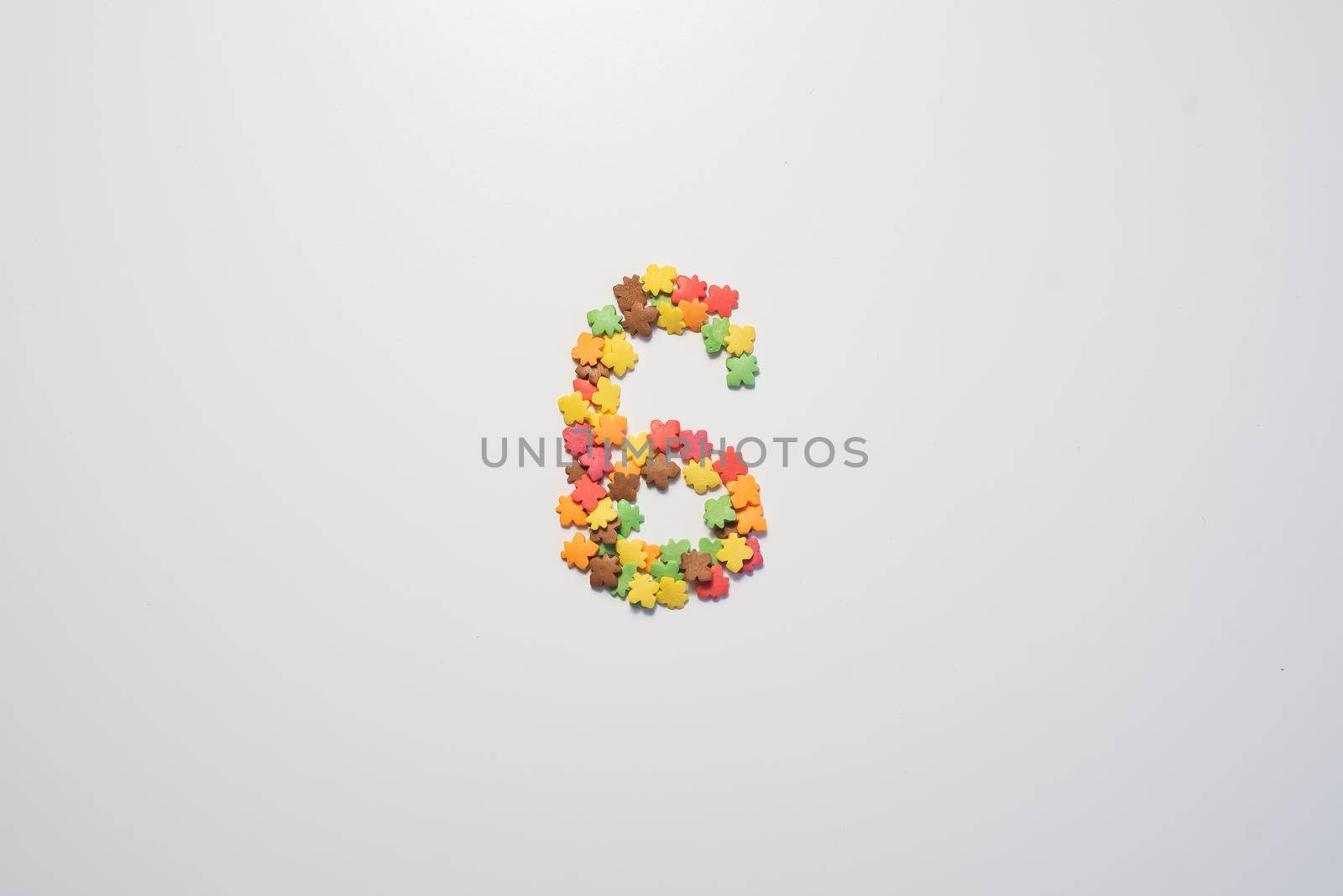 Number six from sweet pastry topping in the form of colorful foliage on a white background