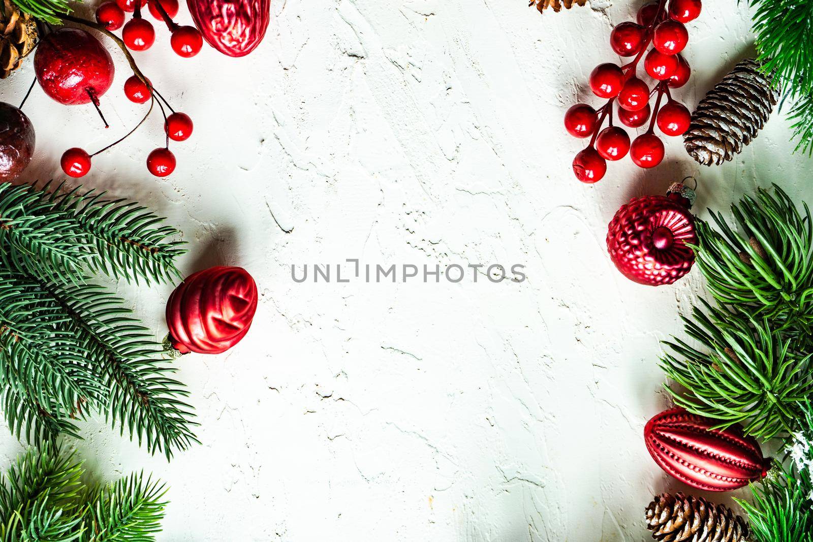 Christmas card concept with frame made with green fir branches, red decoration balls and berries on concrete background