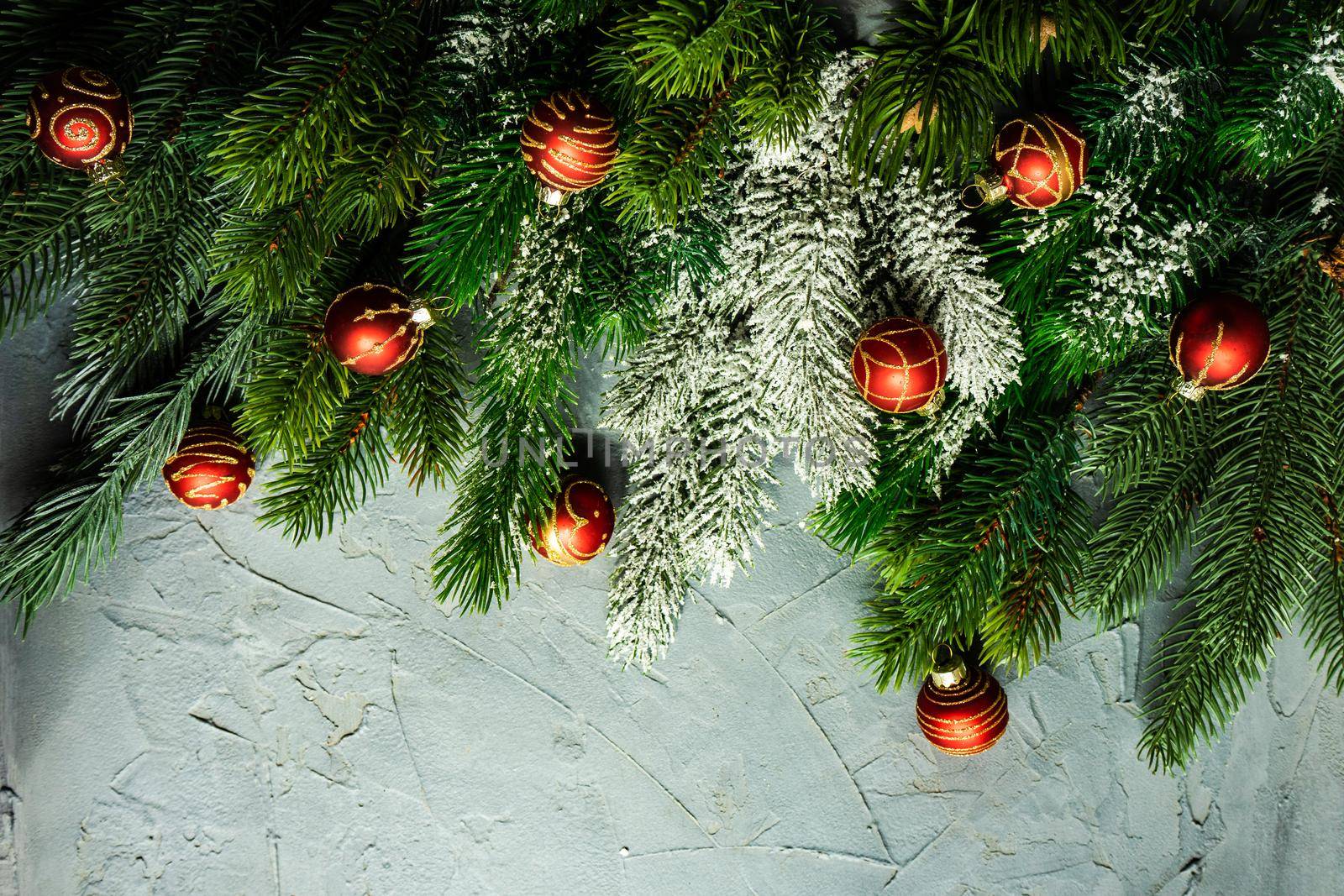Christmas card concept with frame made with green fir branches, red decoration balls and berries on concrete background
