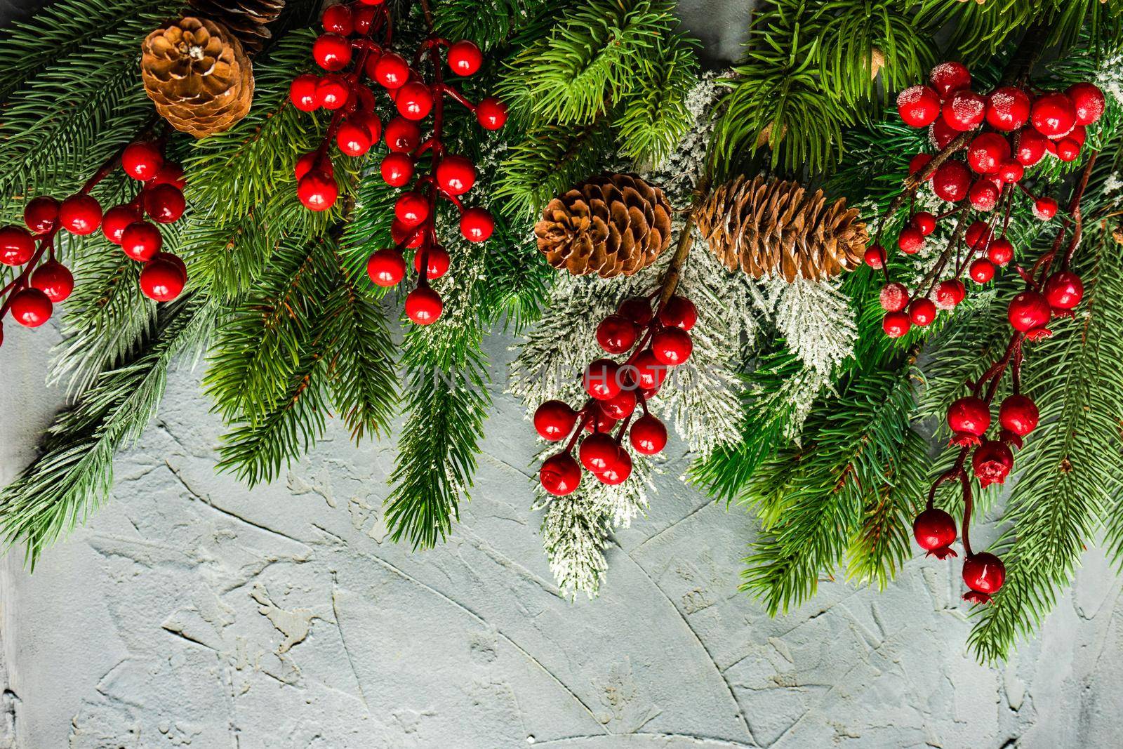 Christmas card concept with frame made with green fir branches, red decoration balls and berries on concrete background