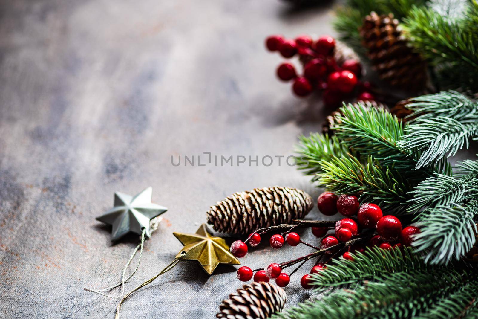 Christmas card concept with frame made with green fir branches, red decoration balls and berries on concrete background