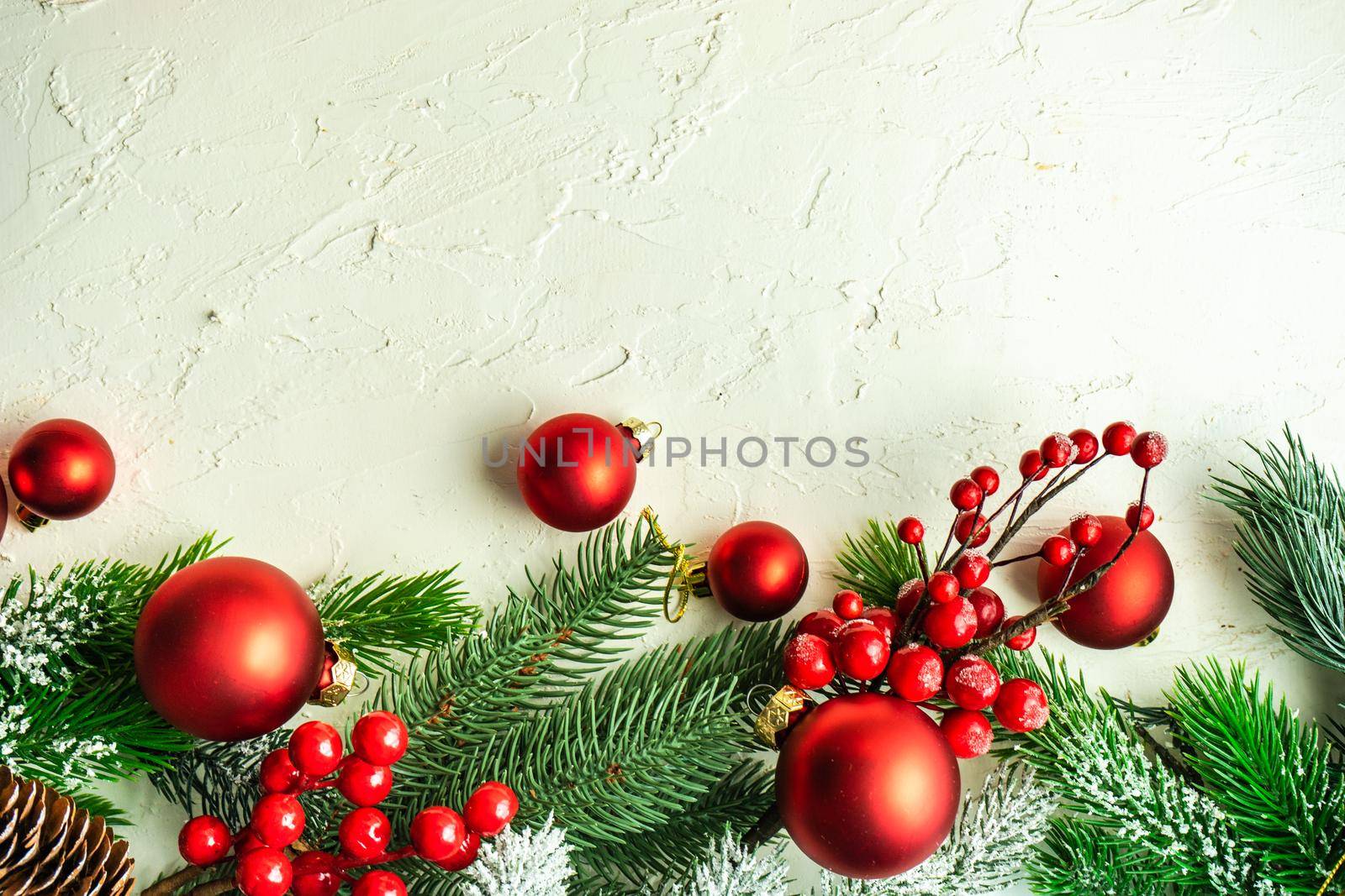 Christmas card concept with frame made with green fir branches, red decoration balls and berries on concrete background