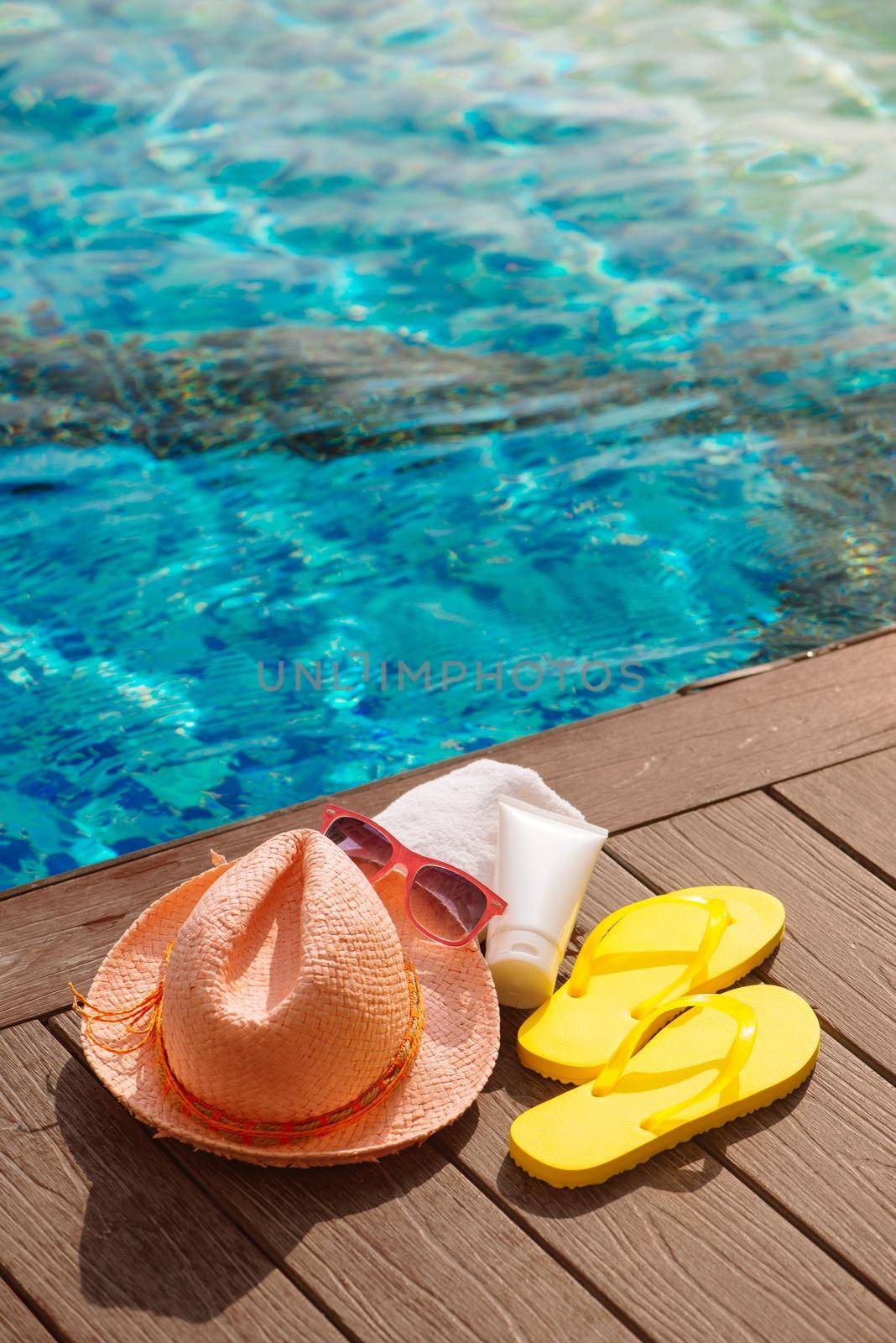 Hat, sunglasses and sunscreen at the side of swimming pool, summer travel concept