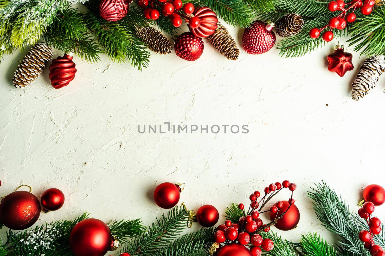 Christmas card concept with frame made with green fir branches, red decoration balls and berries on concrete background