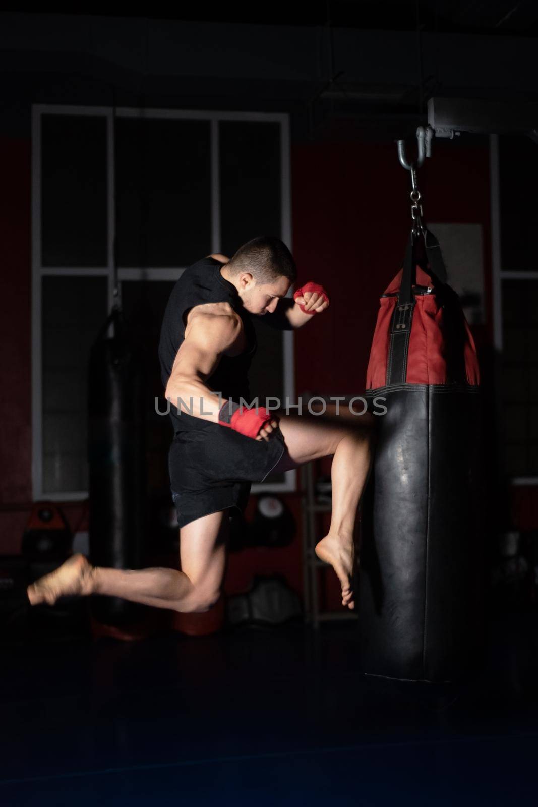 Kickboxing fighter Performing Jumping Air Kicks with Knee on Punch Bag. Caucasian Man Practicing Martial Arts Training at Urban Gym. High quality photo.