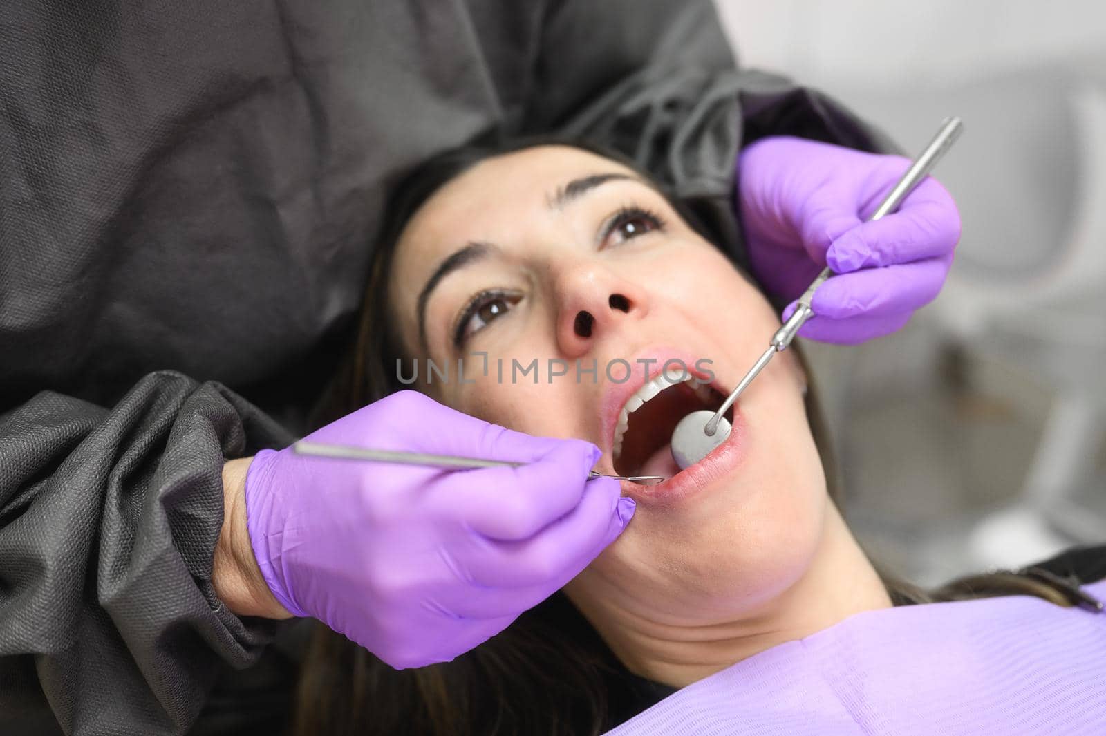 Young female patient visiting dentist office.Beautiful woman sitting at dental chair with open mouth during oral checkup while doctor working at teeth by HERRAEZ