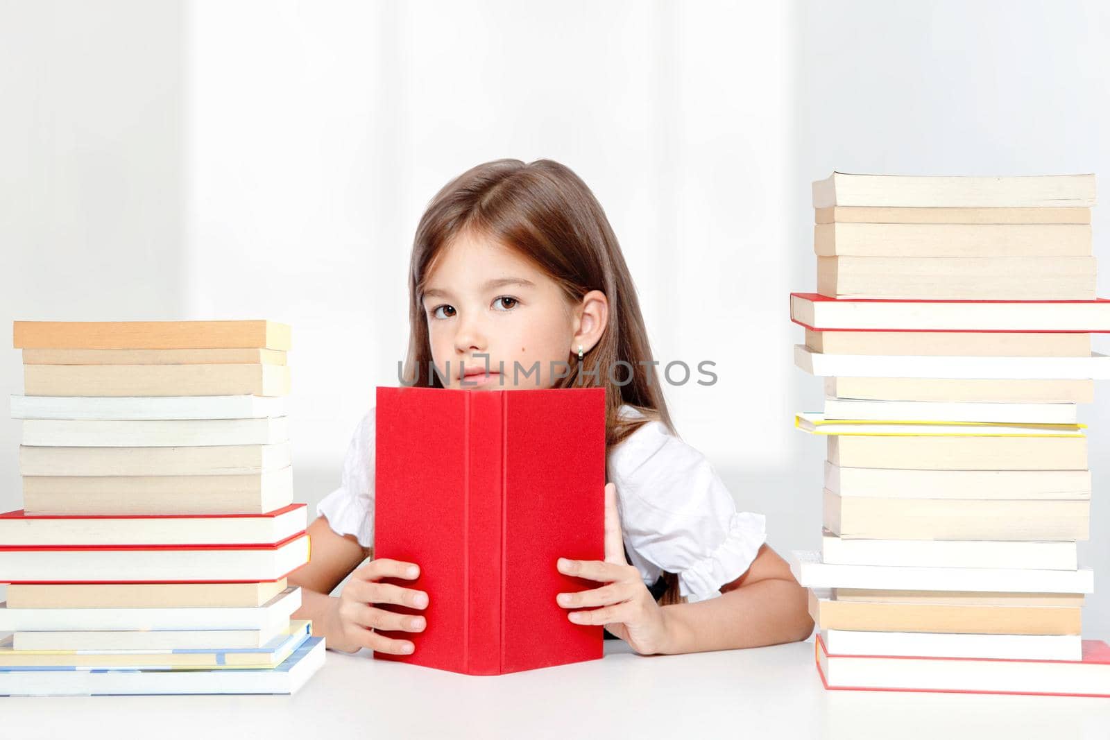 Young cute girl sitting at the table and reading a book by Taut