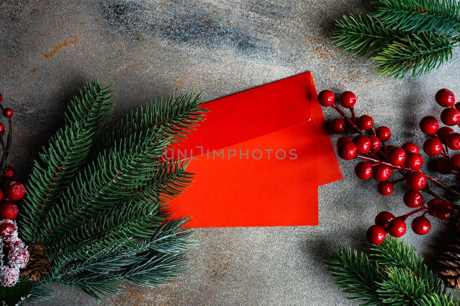 Christmas card concept with frame made with green fir branches, red decoration balls and berries on concrete background