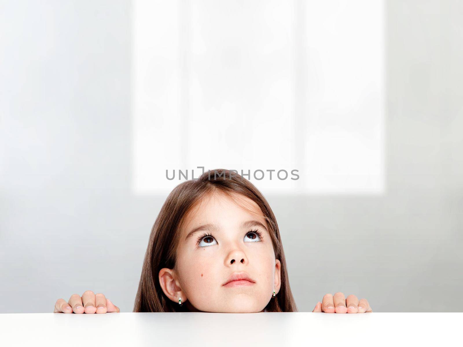 Cute little child girl looking up on the desk at school. by Taut