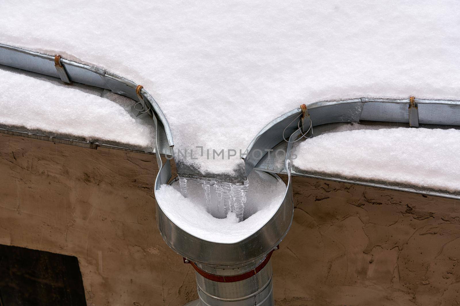 Snow and frozen water blocked the drain on the roof of the old house. Close up