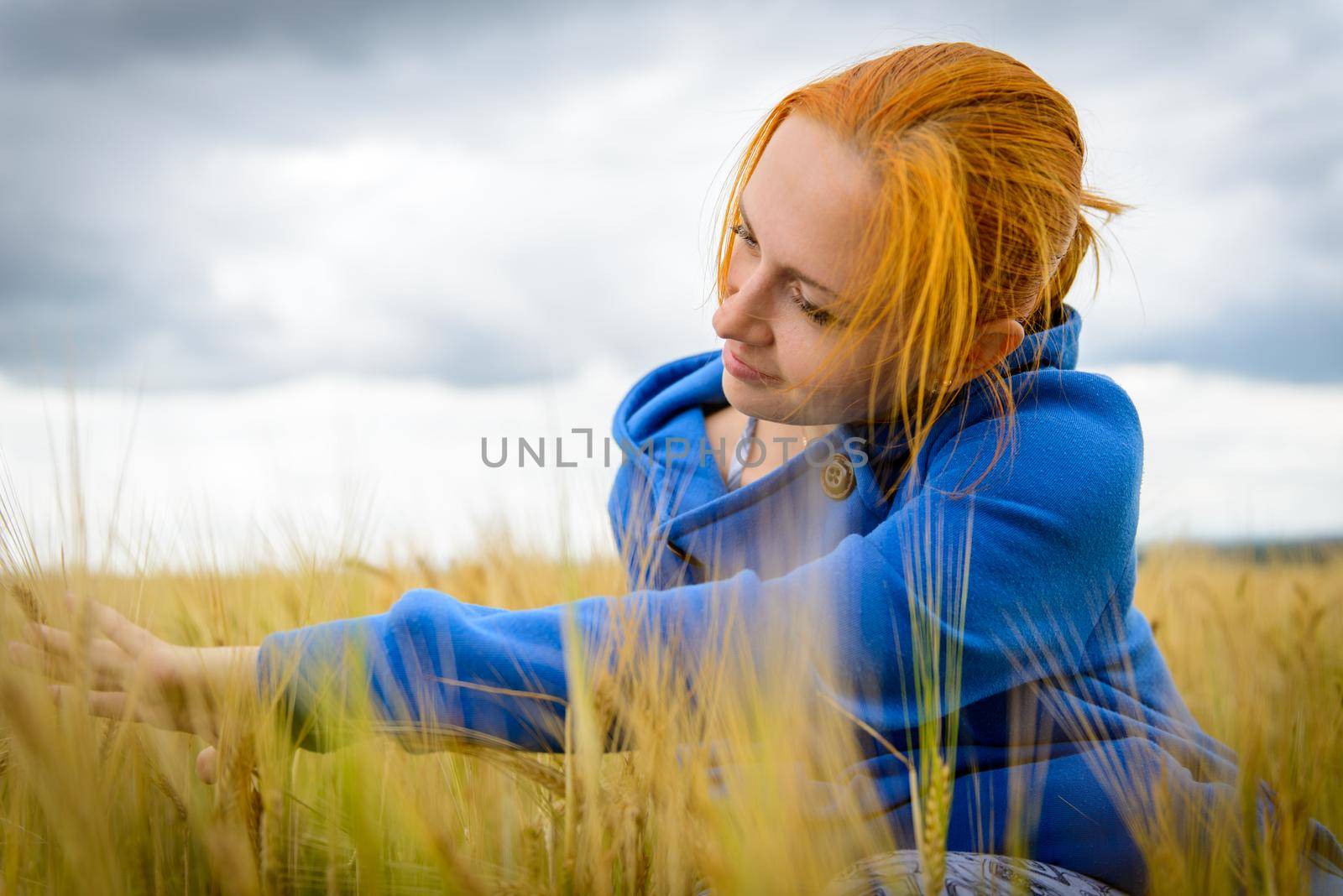 Young woman wearing blue sweater in wheat field on a cloudy day