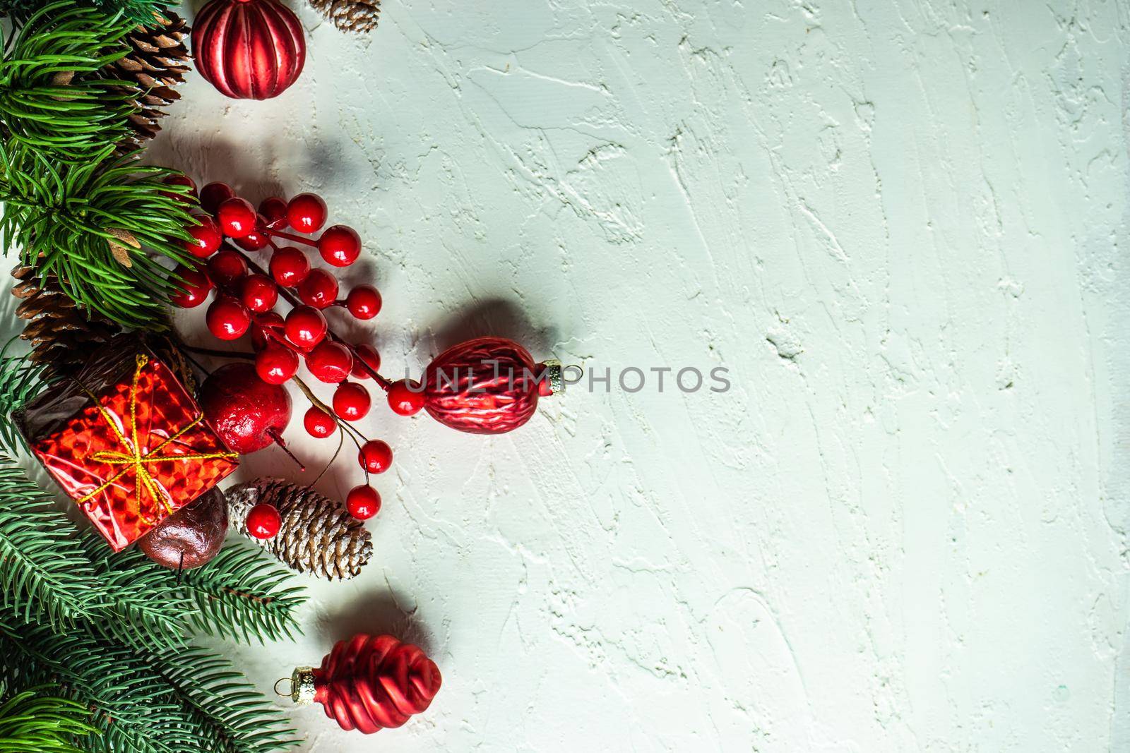 Christmas card concept with frame made with green fir branches, red decoration balls and berries on concrete background