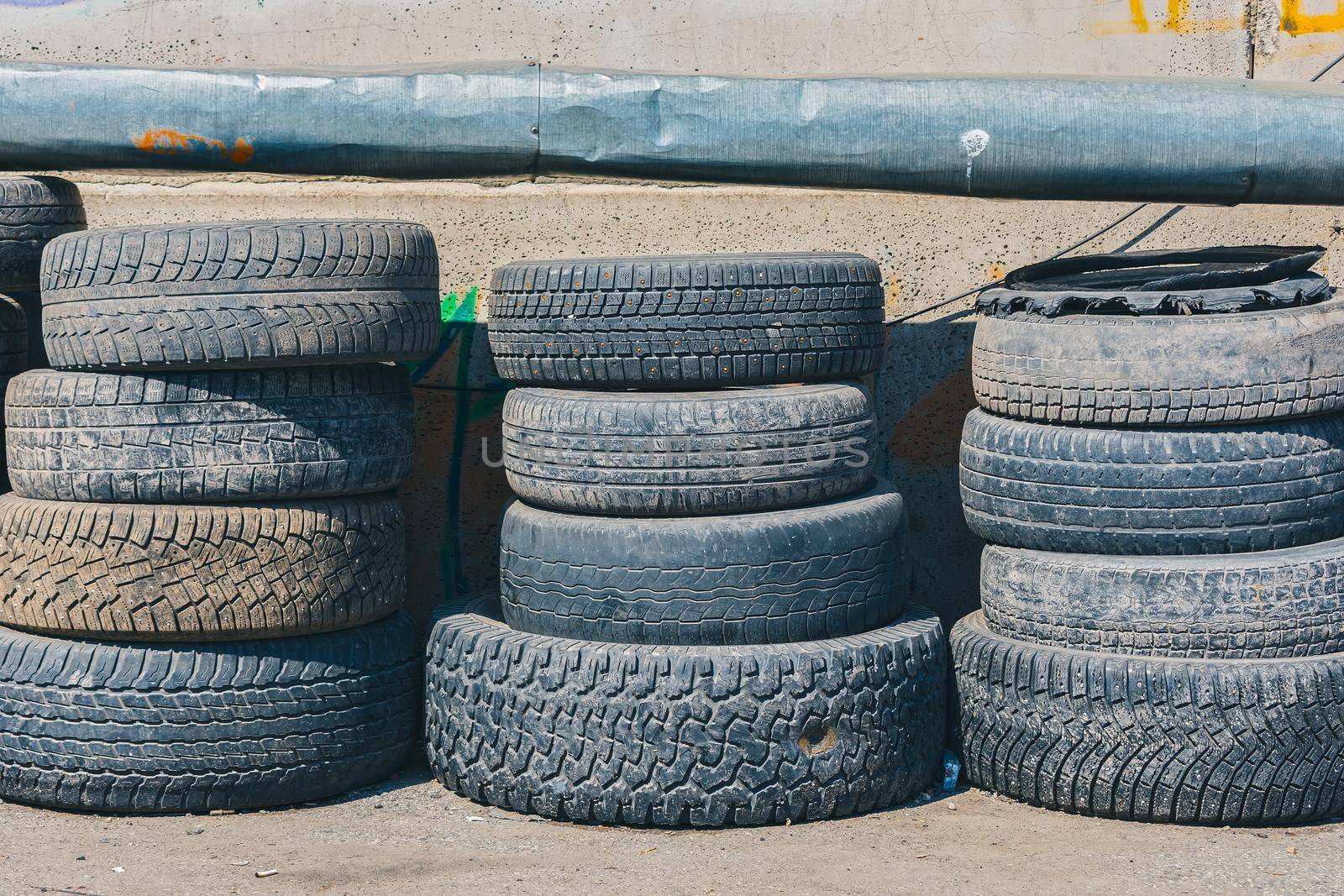 Many different used tires are piled up against a wall in a landfill for further recycling