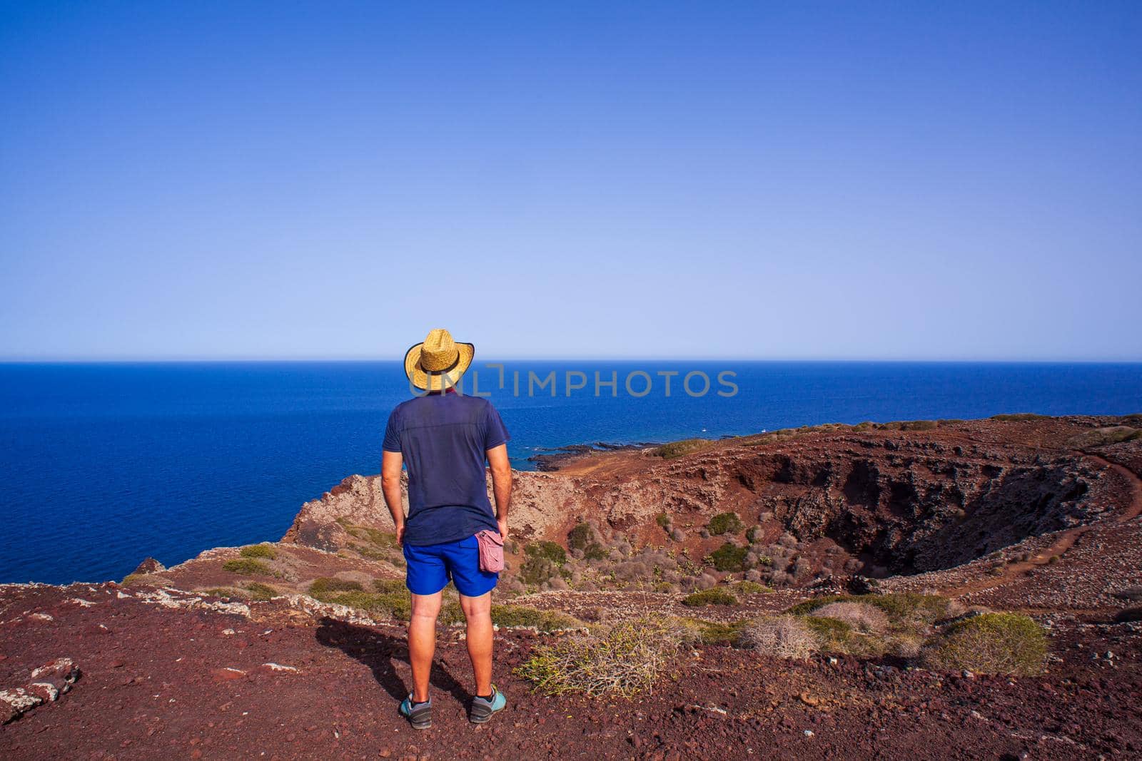 A man with a straw hat looking the sea from the top of the volcano called Monte Nero, Linosa. Sicily. Italy