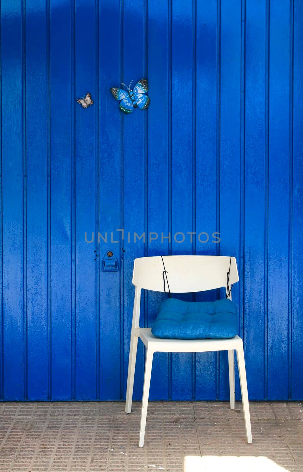 Colorful blue metallic door with two decorative butterflies and white chair