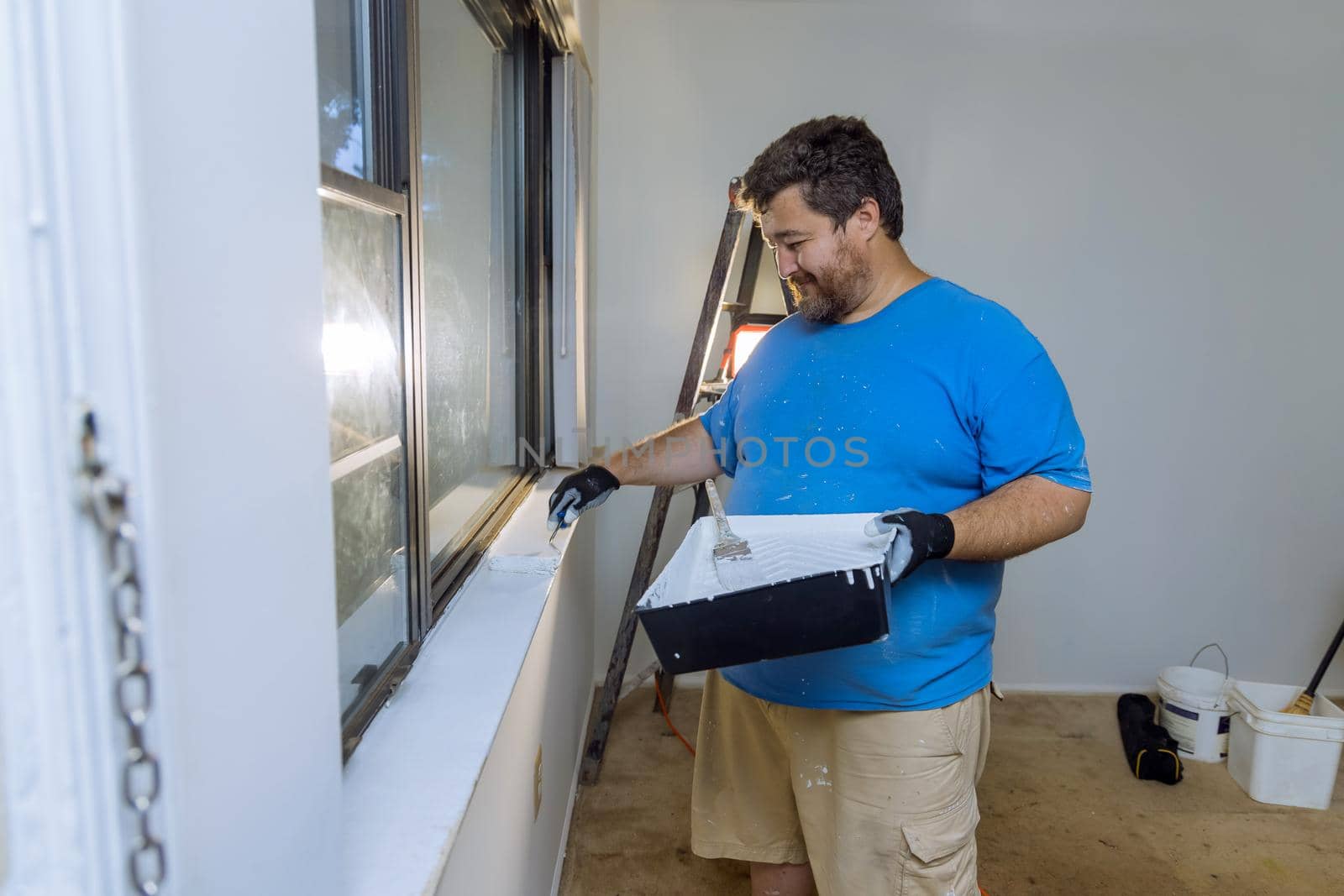Handyman paints a window molding frame with a paint roller at home renovation
