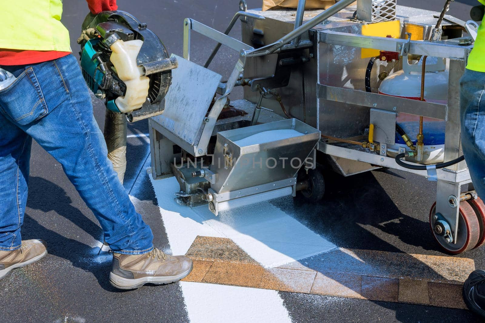 Workers apply a road marking to the stripe with white paint and sprinkle the stripes with a reflective powder on the asphalt by ungvar