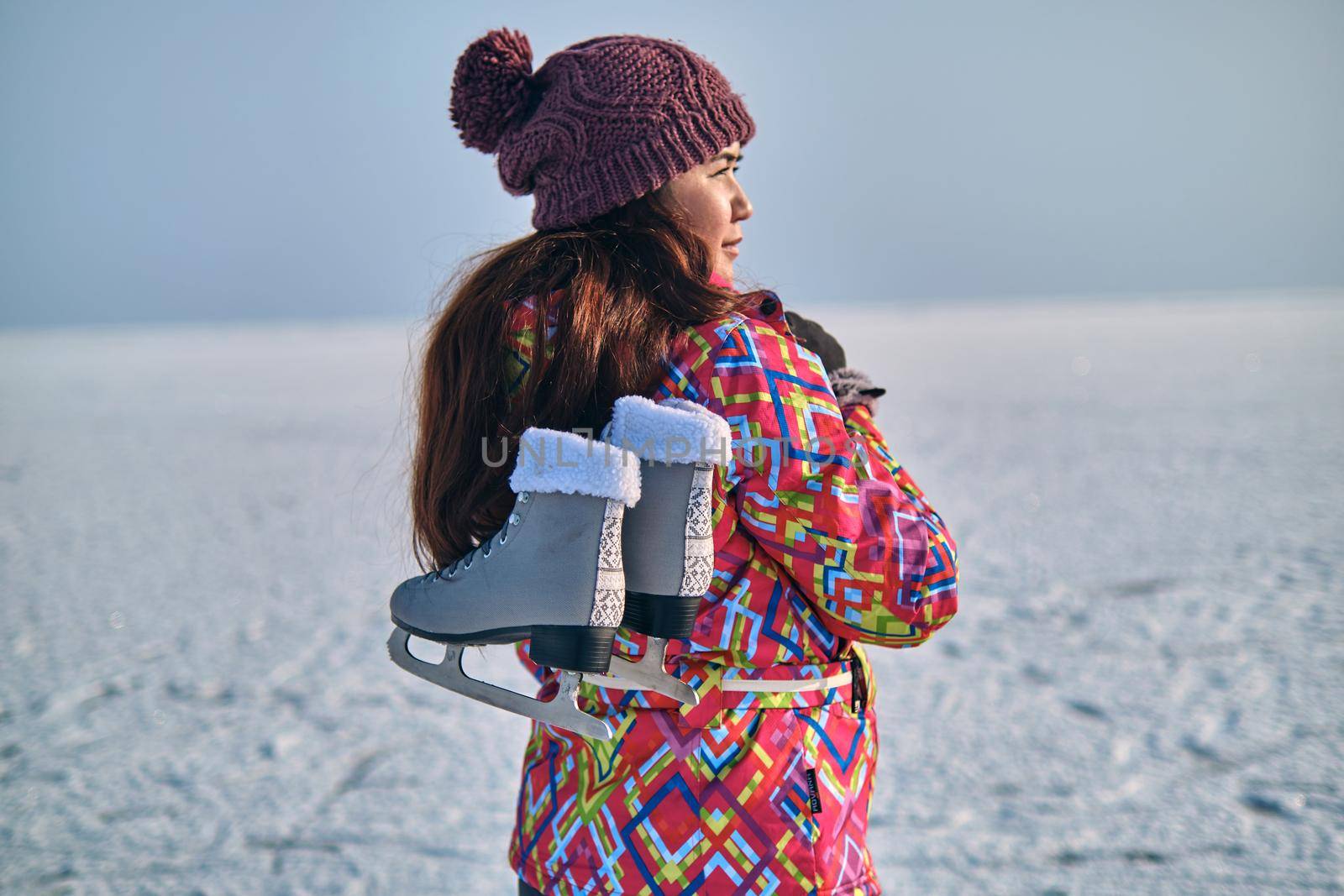 A woman holds skates on her shoulder after skiing on a frozen lake by snep_photo