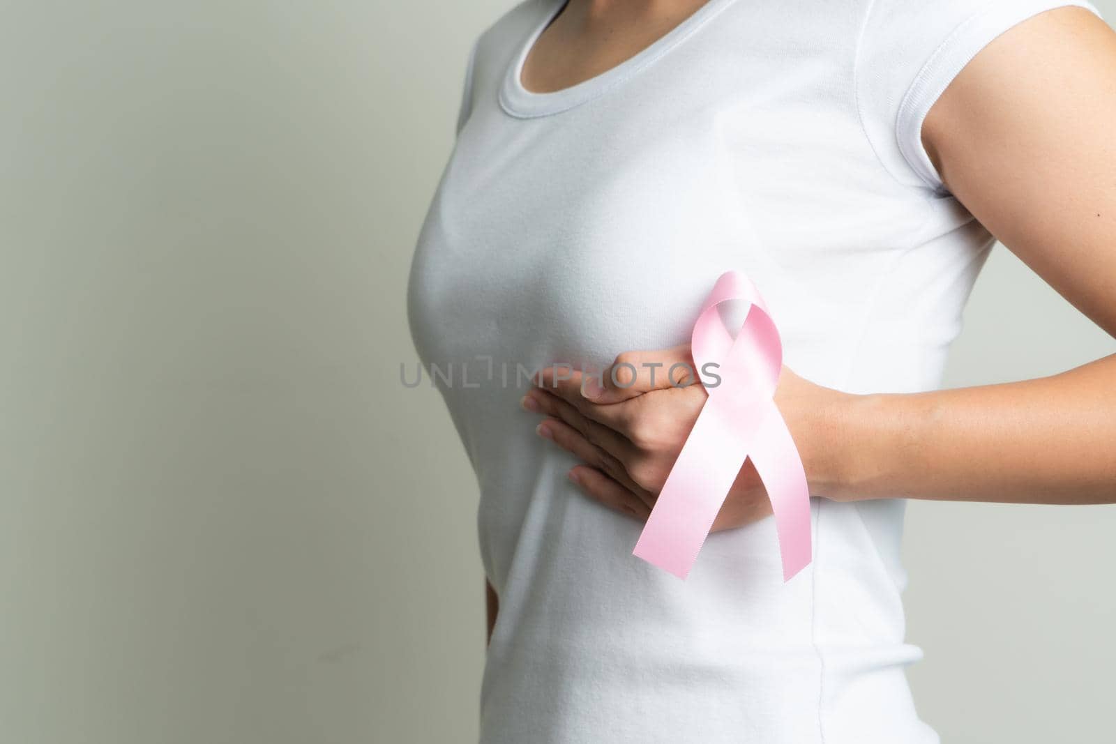 pink badge ribbon on woman hand touching chest to support breast cancer cause. breast cancer awareness concept by psodaz