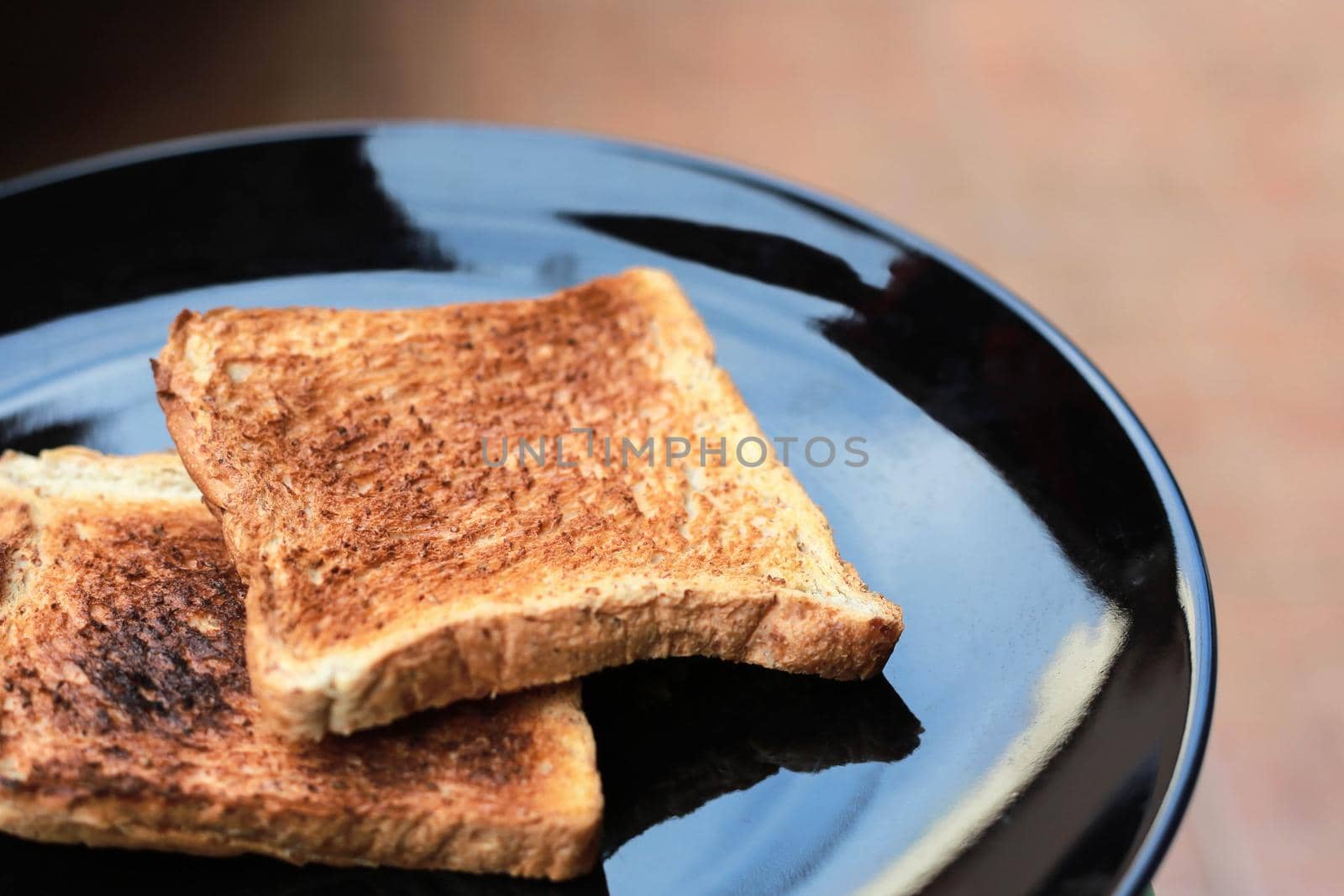 Slice toasted bread on black dish. by jayzynism
