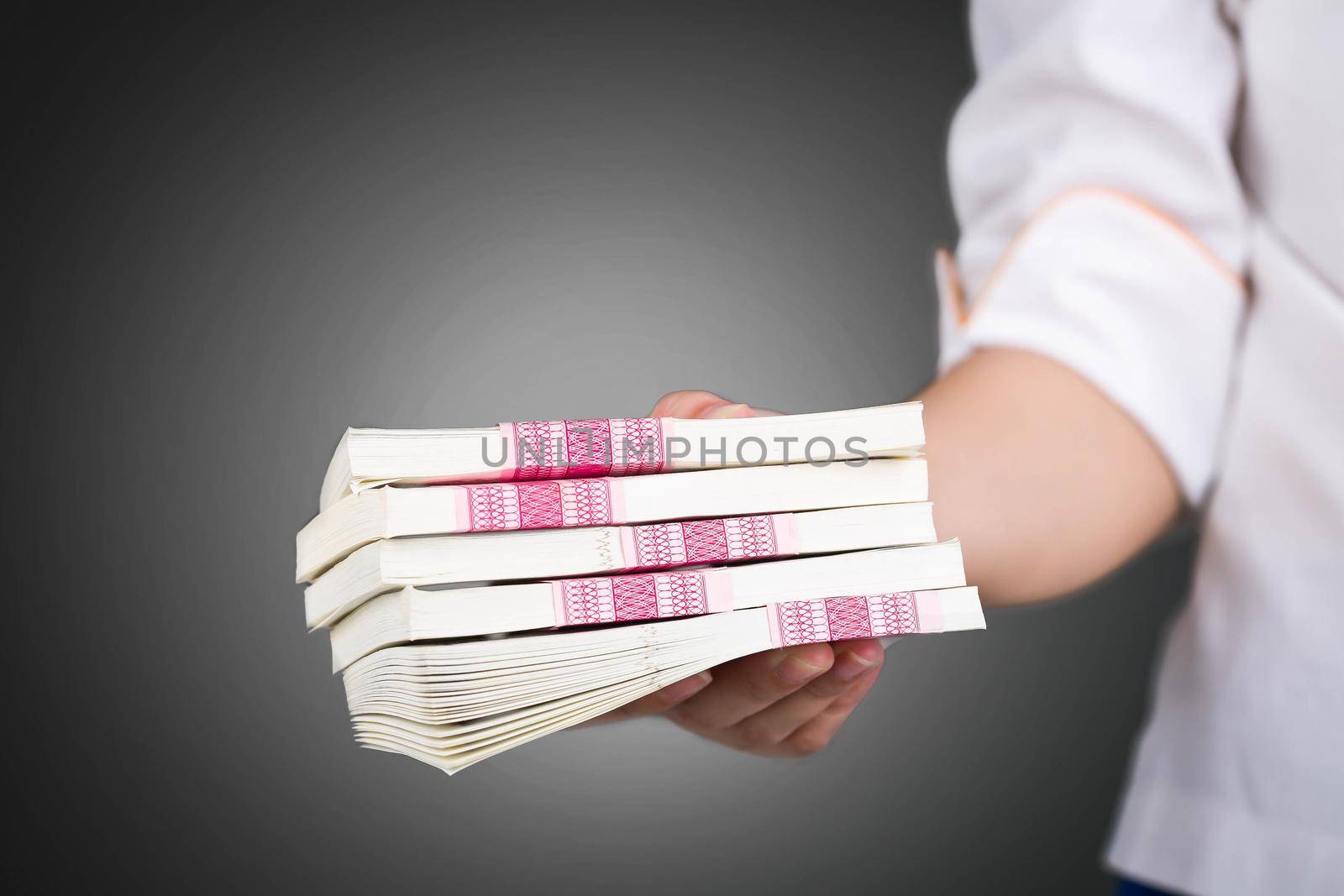 Female hand giving money pack on black background.