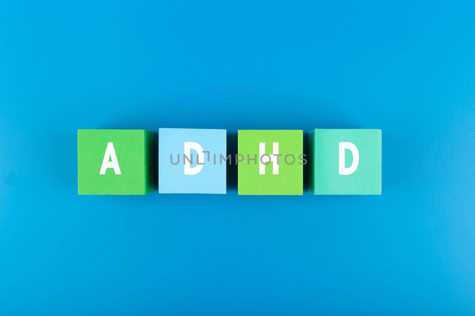 Minimal modern concept of Adhd in blue color. Top view of multicolored blocks with written Adhd letters against blue background with light gradient