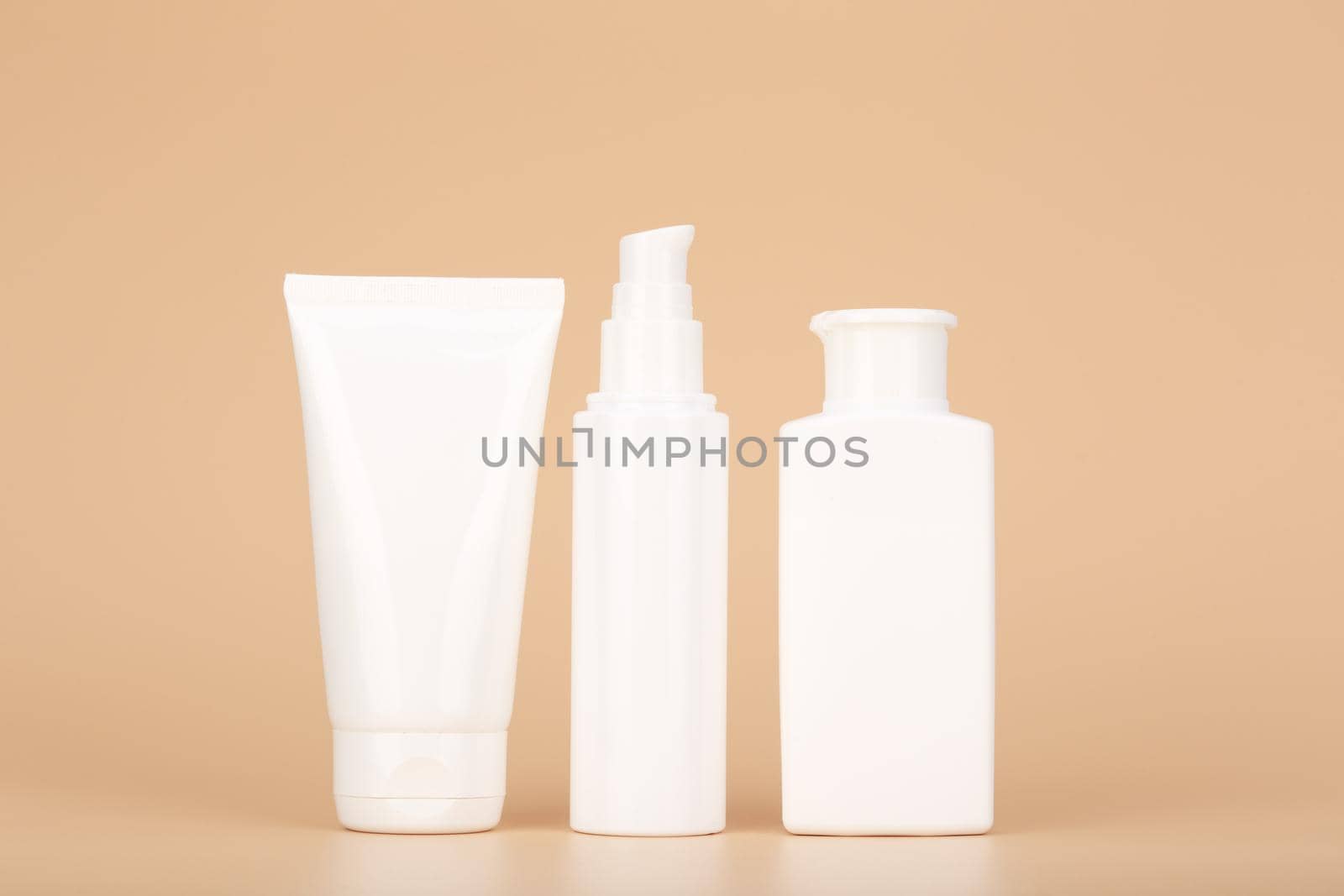 Set of white unbranded cosmetic tubes for face and body care in a row against pastel beige background. Concept of organic, natural, eco friendly cosmetics and beauty products for daily skin care