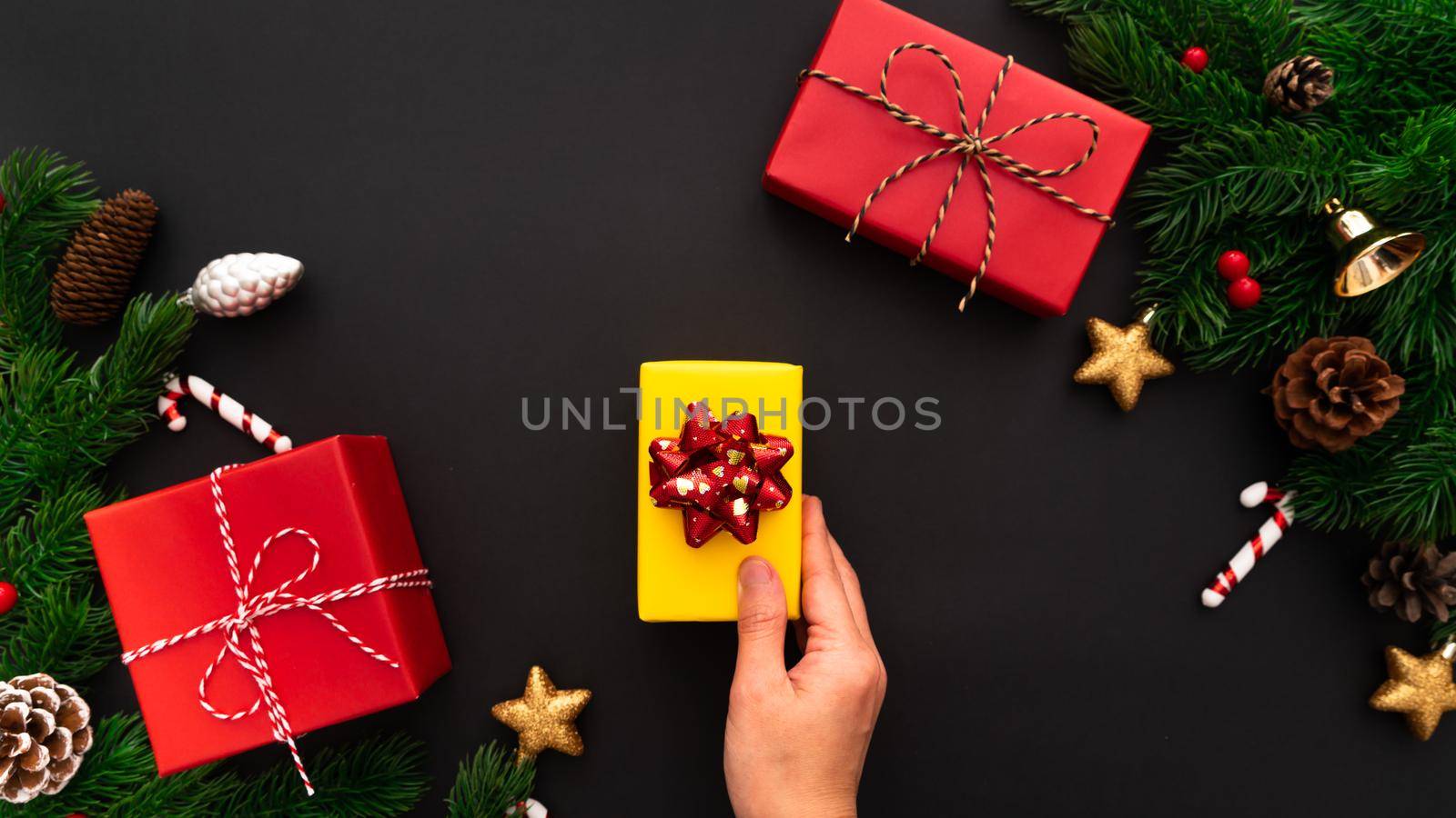 hand holding Christmas gift box and pine tree with xmas decoration on black background