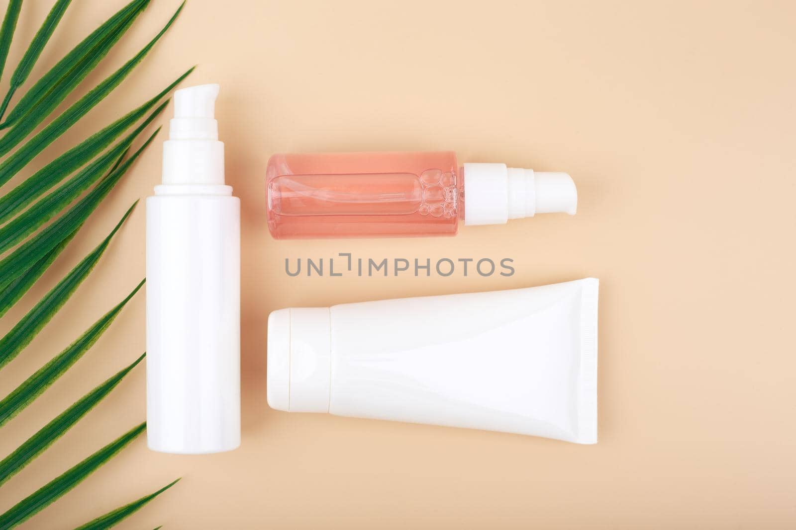 Cosmetic tubes with beauty products for skin care on beige background decorated with palm leaf. Concept of organic, eco friendly beauty products with natural ingredients