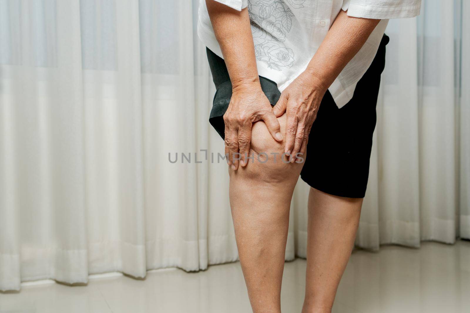 senior woman suffering from knee pain at home, health problem concept by psodaz