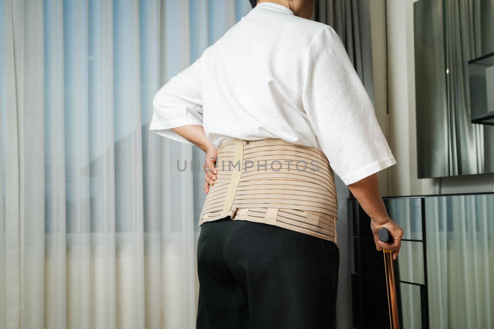 Senior back pain woman with walking stick at home by psodaz