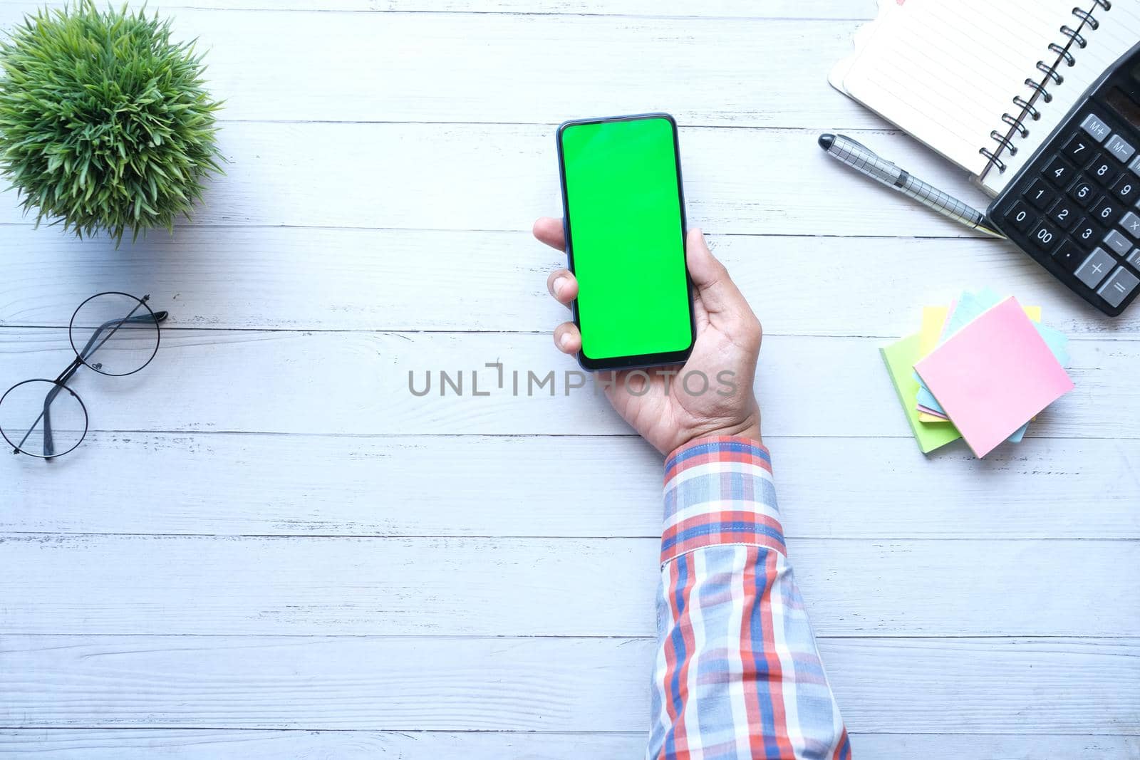 Top view of man hand holding smart phone with empty screen on office desk .