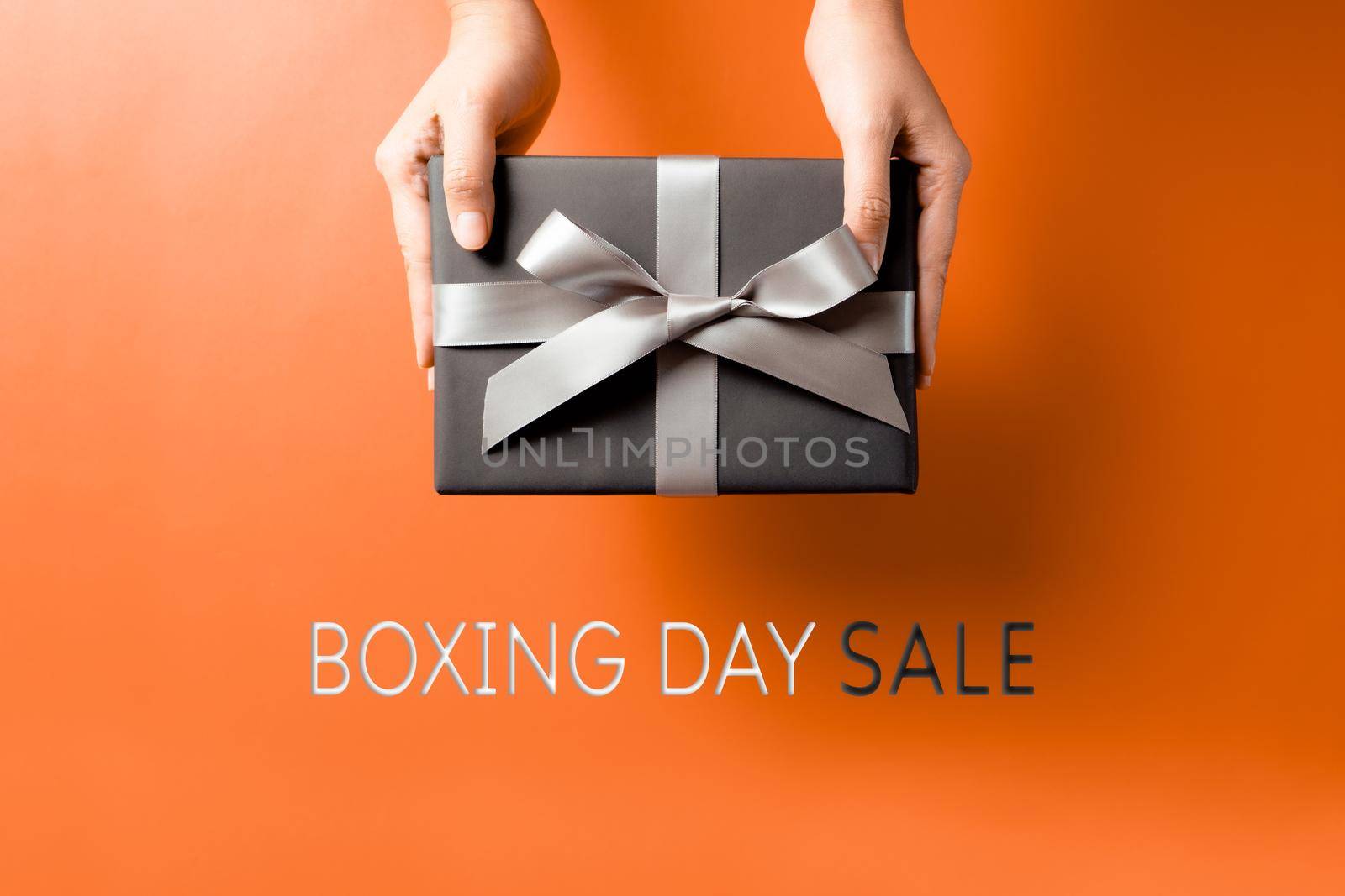 Boxing Day sale, young woman hand with a gift box offer to receiver by psodaz