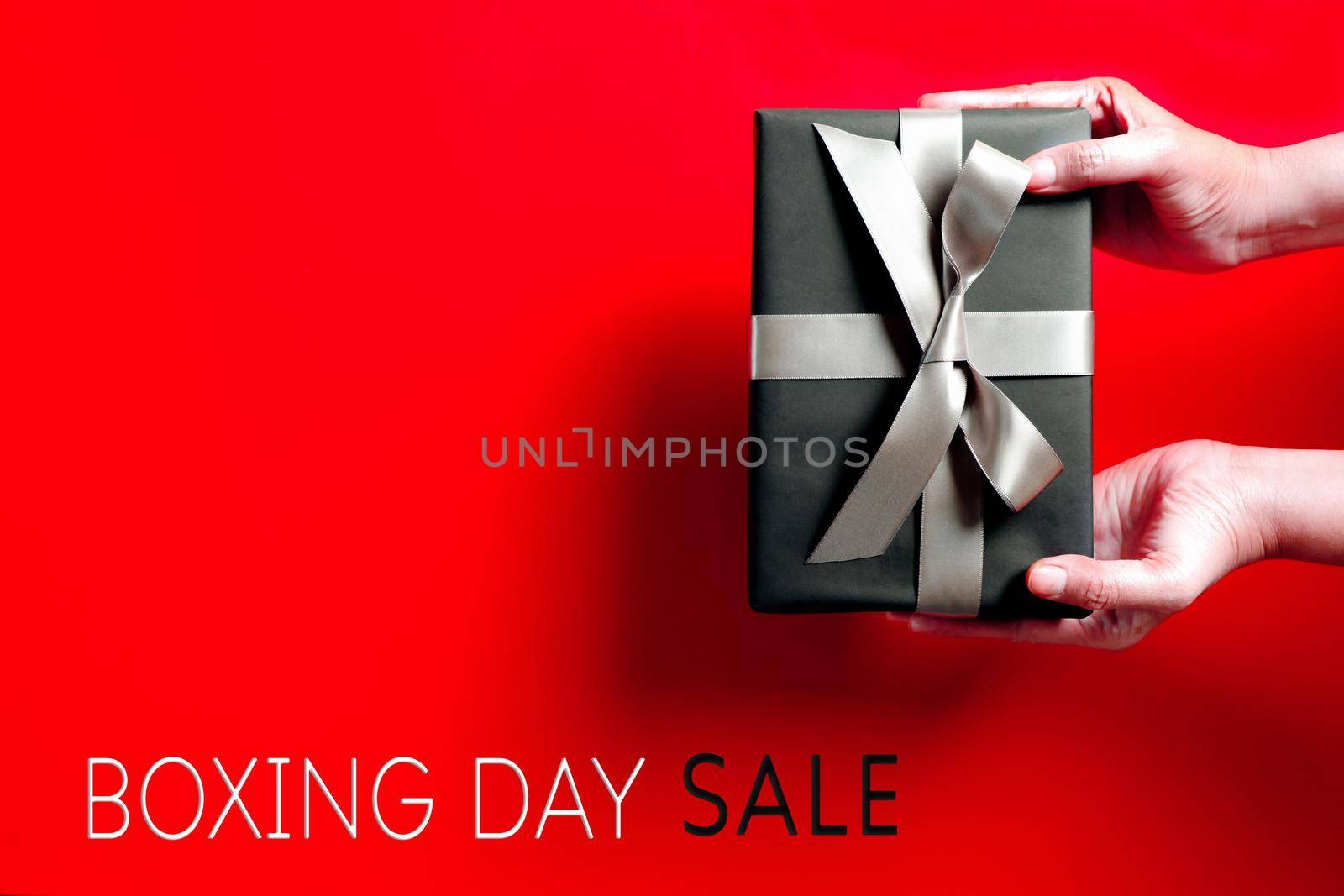 Boxing Day sale, young woman hand with a gift box offer to receiver by psodaz