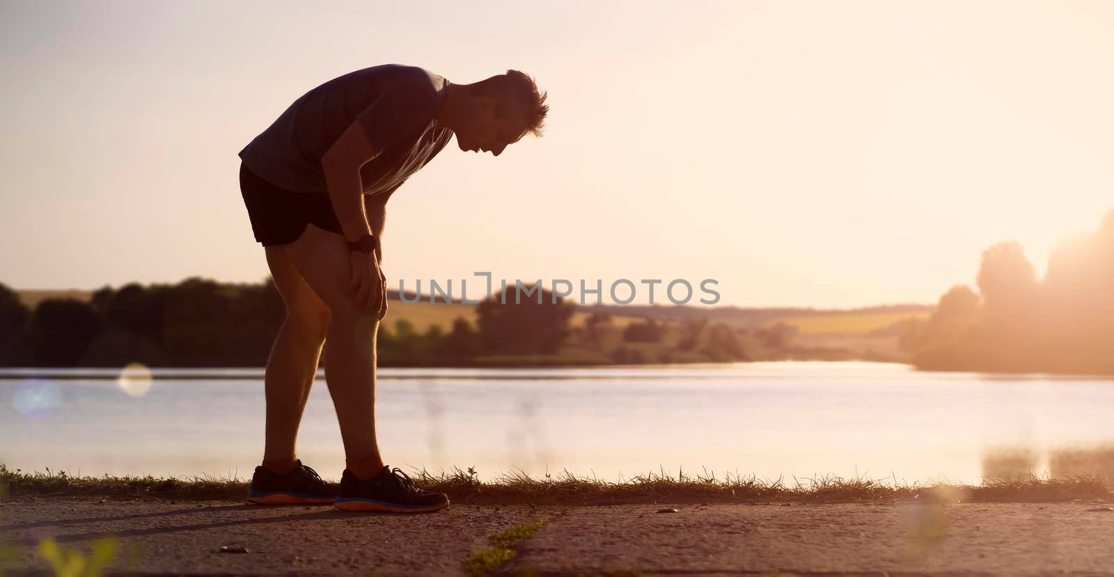 A young man jogging at sunset by the lake. by africapink