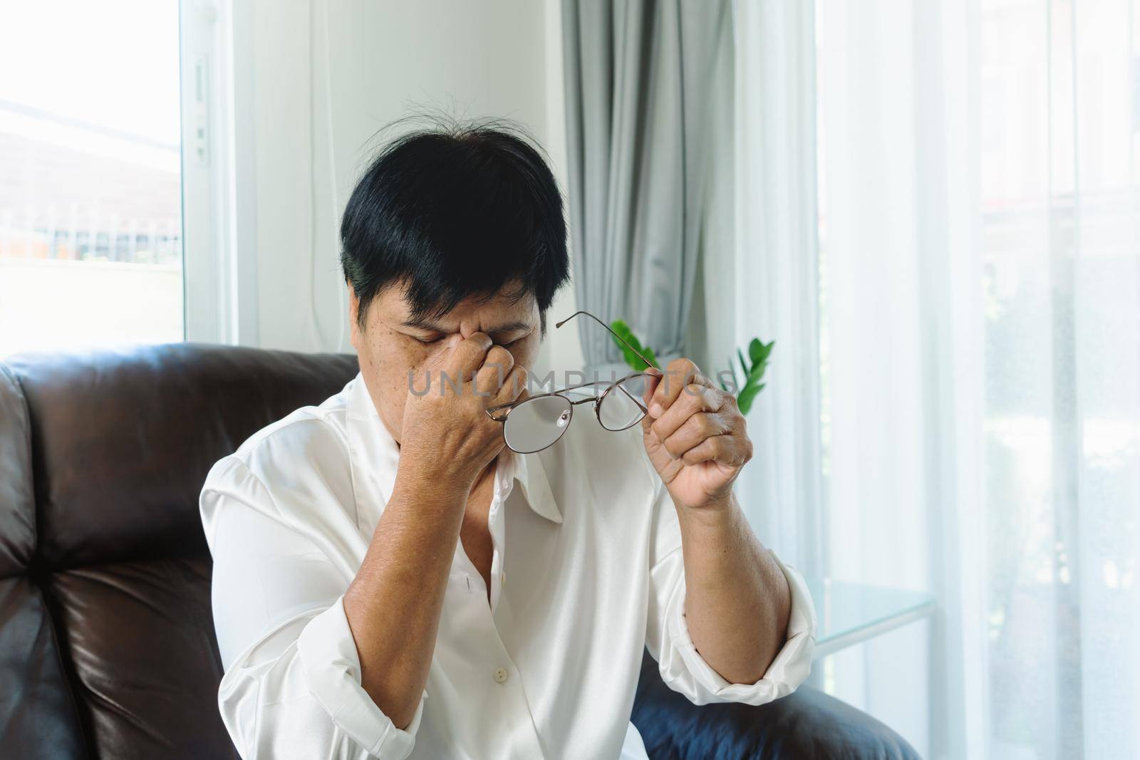 Tired old woman removing eyeglasses, massaging eyes after reading paper book. feeling discomfort because of long wearing glasses, suffering from eyes pain or headache