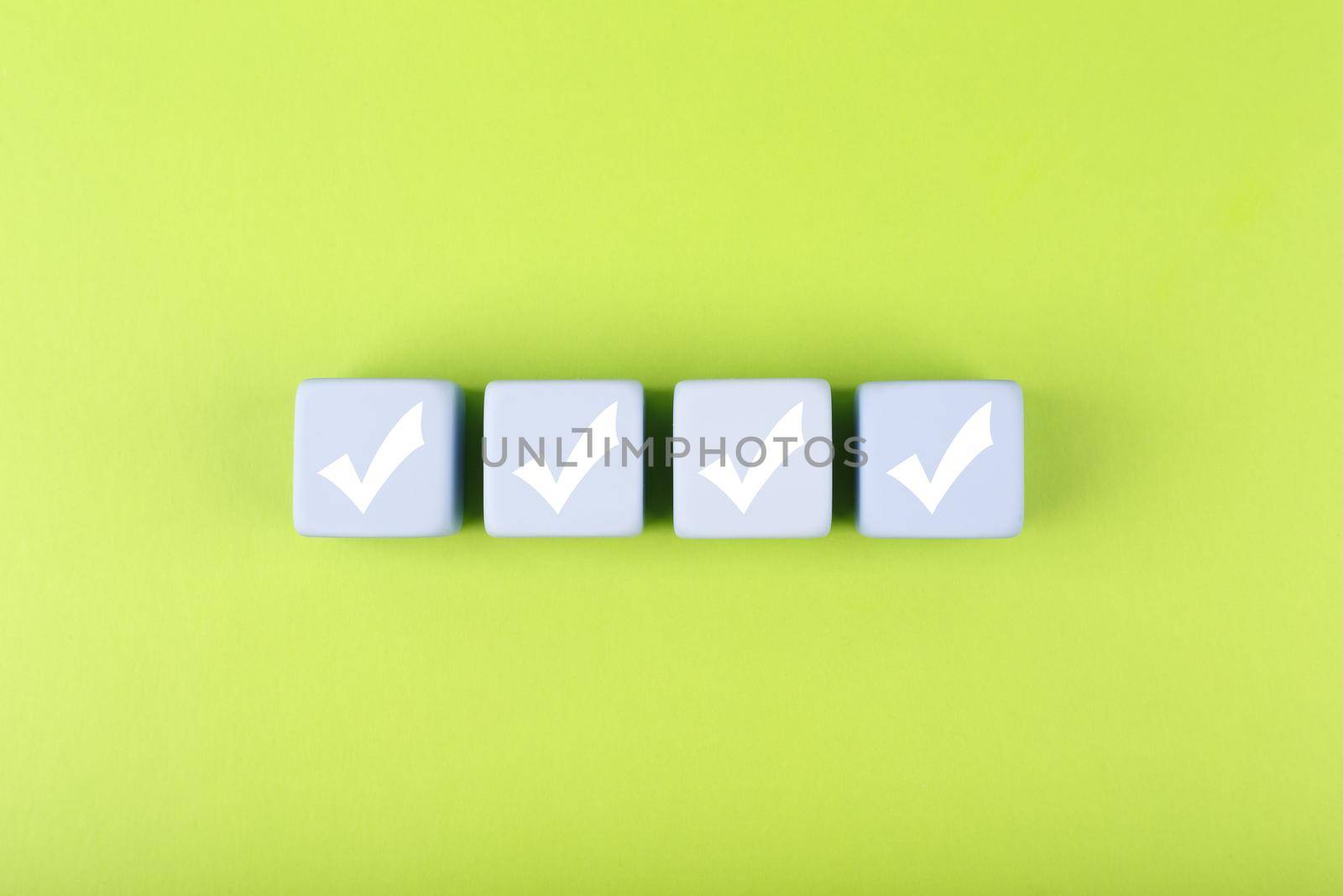 Four checkmarks on white cubes against bright green background. Concept of questionary, checklist, to do list, planning, business or verification. Creative minimal composition