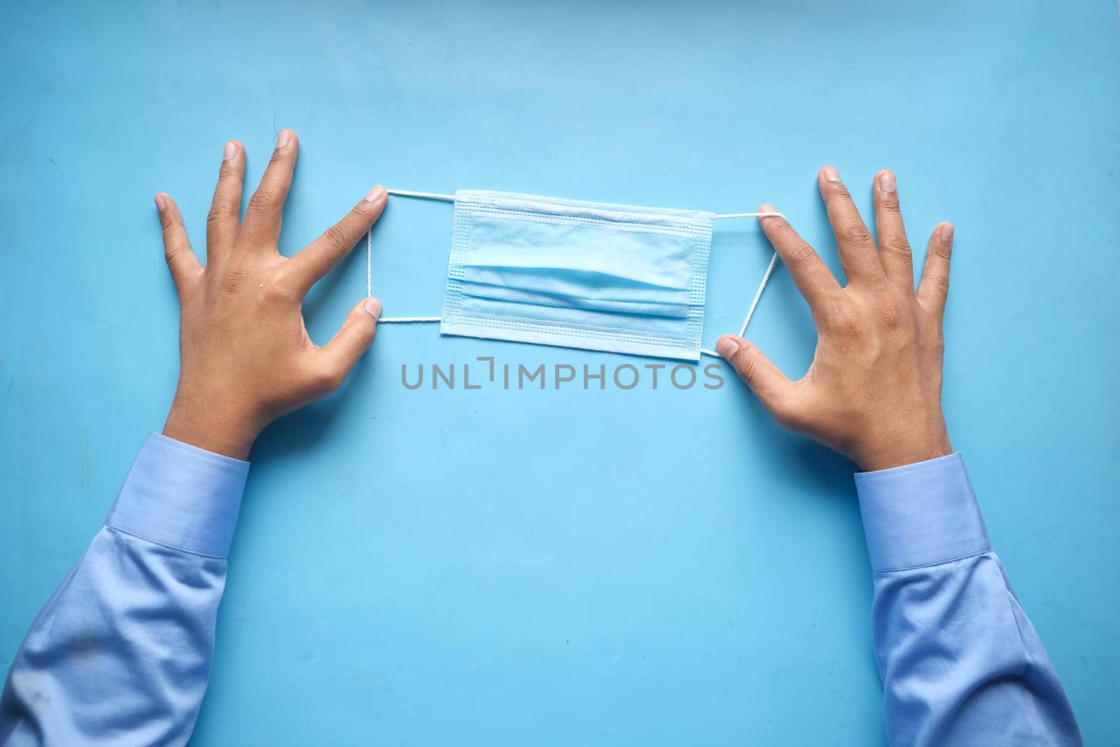 man hand holding surgical face mask on blue background
