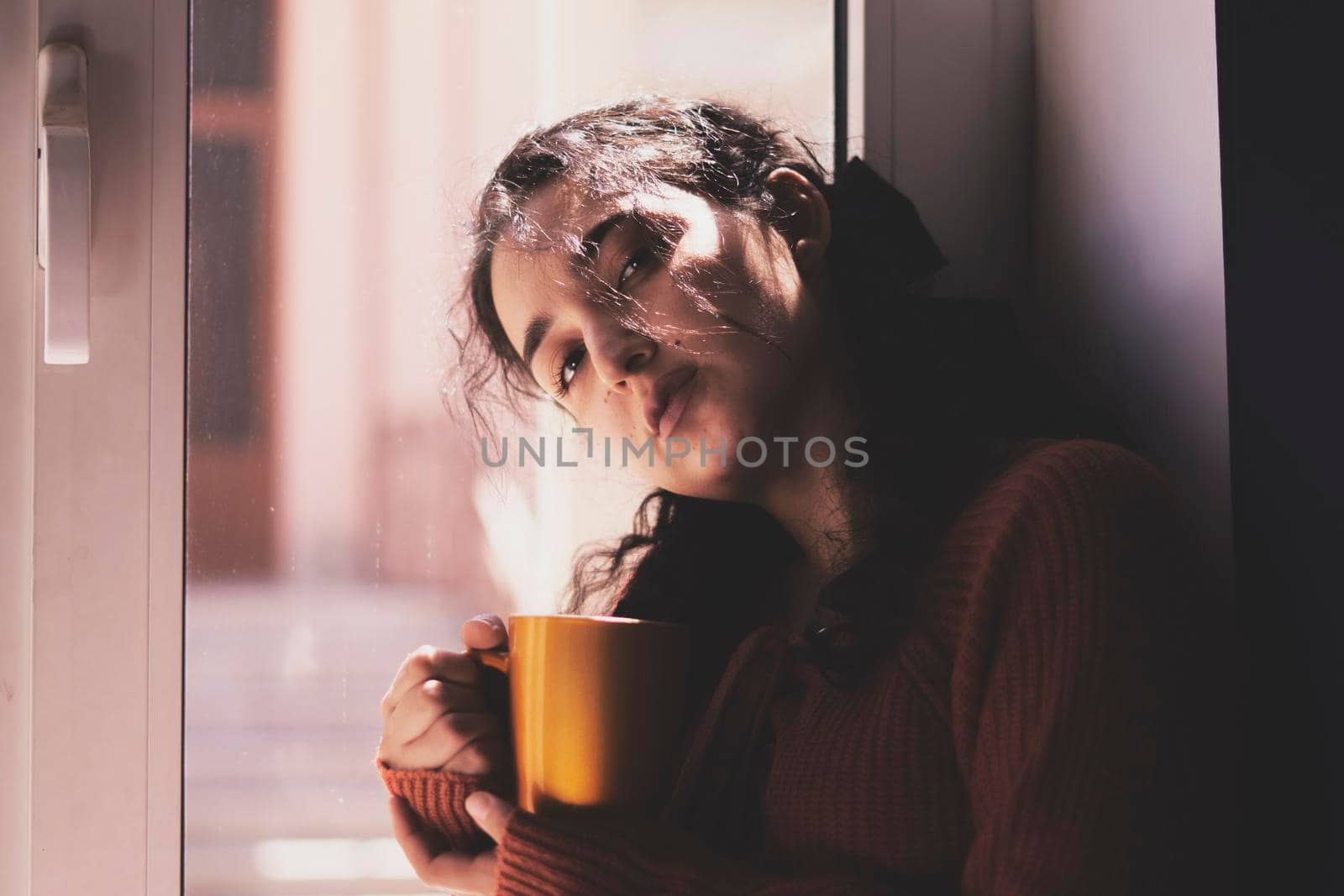 Cold autumn days - a young multi-racial female drinks coffee in a cozy windowsill. Middle-eastern or mixed-race woman enjoys weekend drinking hot tea near the windows