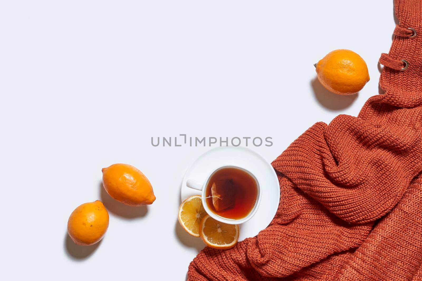 Autumn background with tea and knitted sweater on white background. Hot herbal lemon tea with orange warming pullover on white background. Fall background