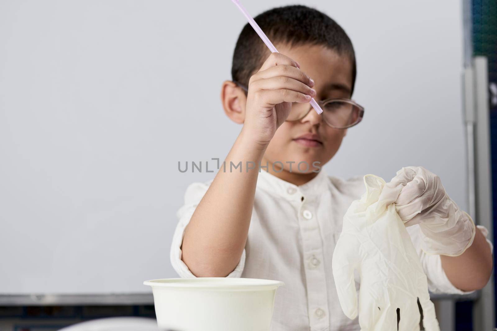 Little boy scientist in white making experiments against the white background