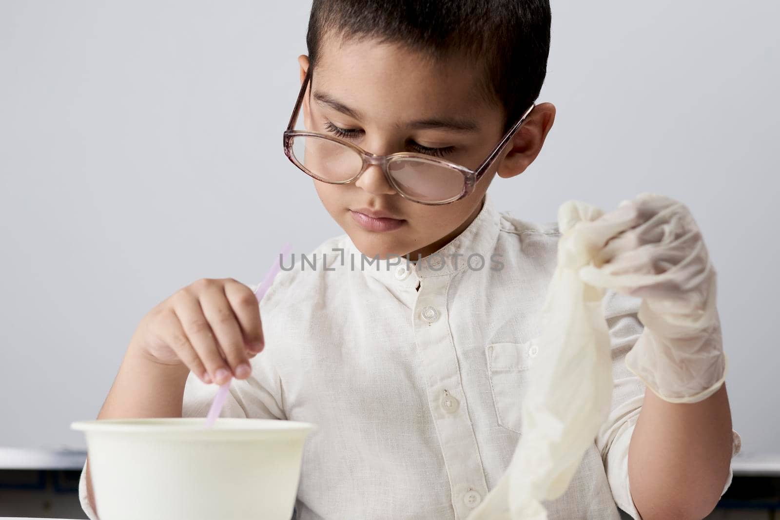 Portrait of a cute kid in eyeglasses experimenting with liquids against the white background