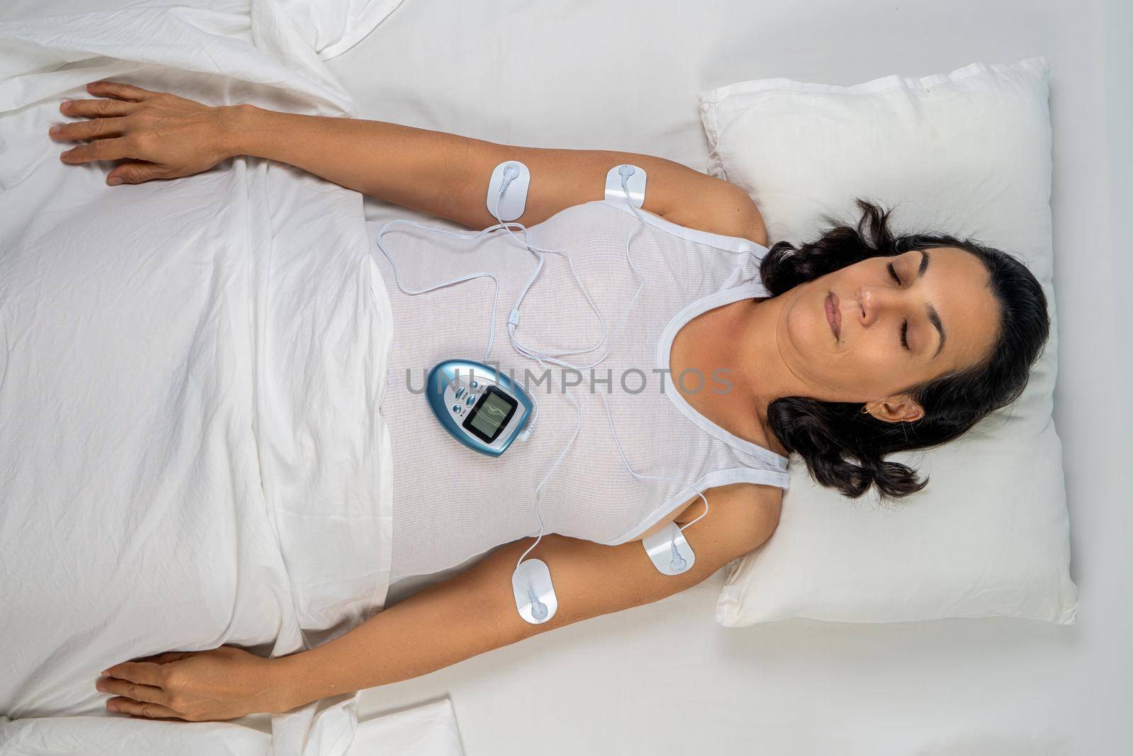 Woman lying on her back with four sensors that connect her to an electro massage equipment