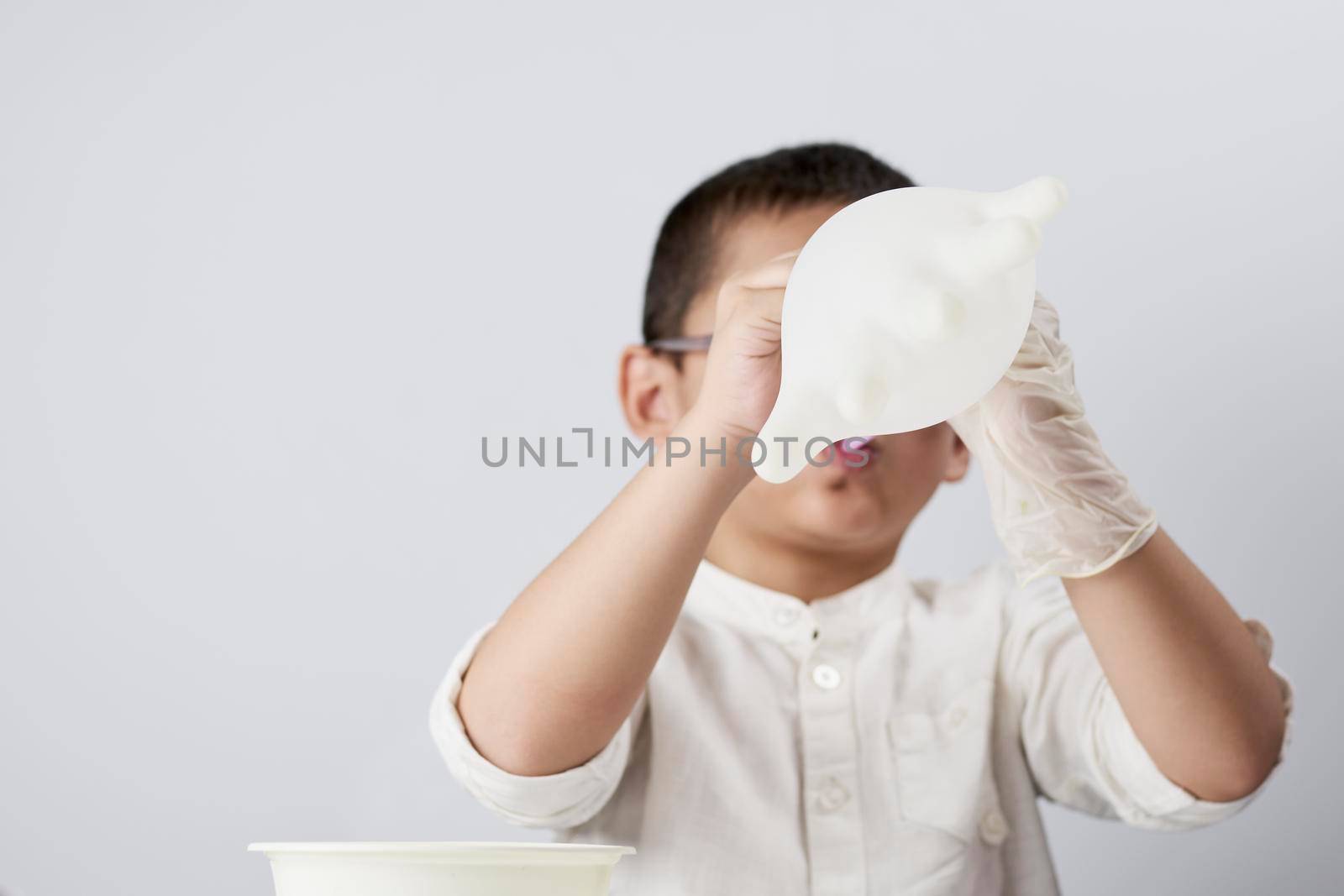 A little kid blowing medical gloves as balloon against the white background