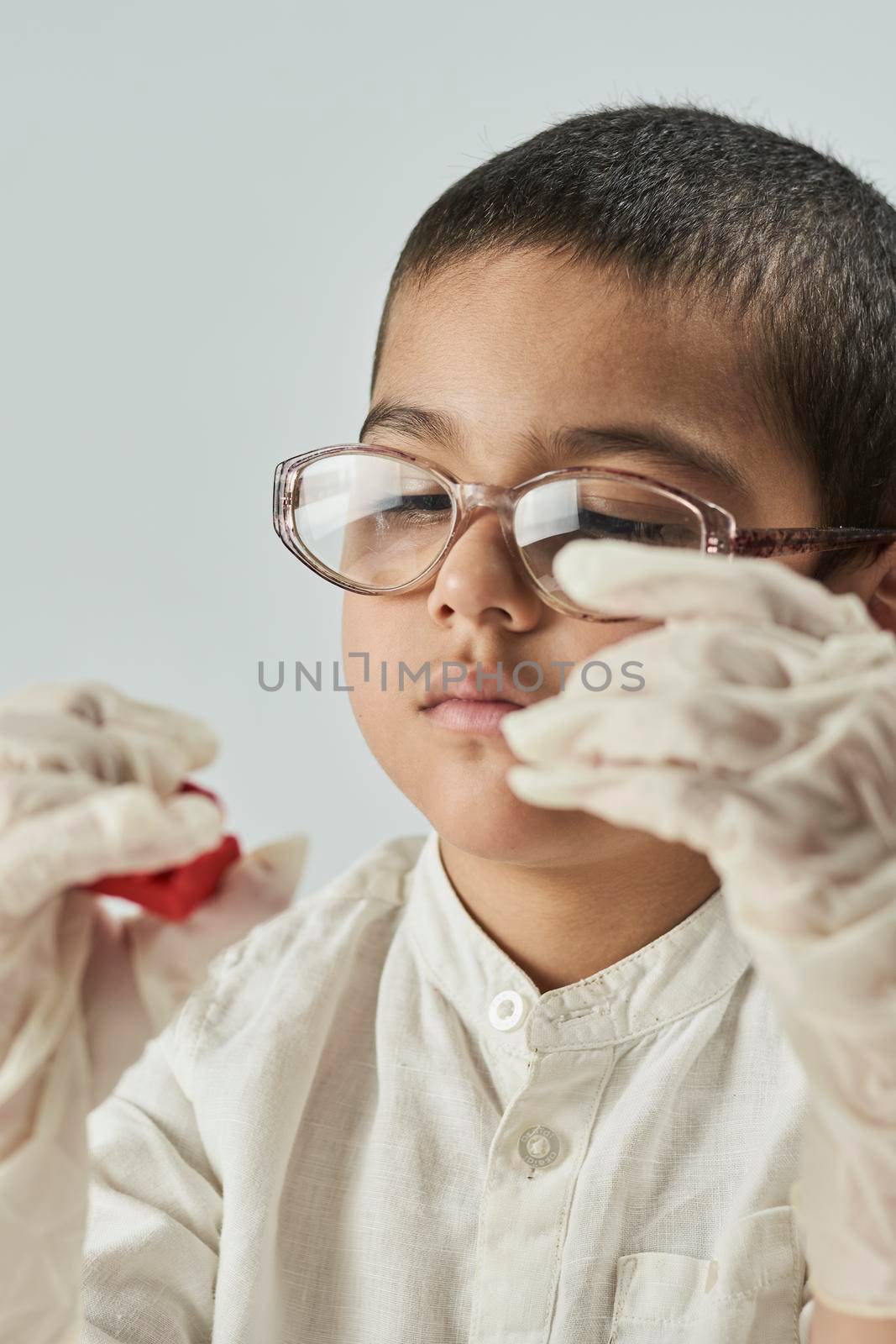 Close-up portrait of mixed raced child in glasses and gloves experimenting with slime