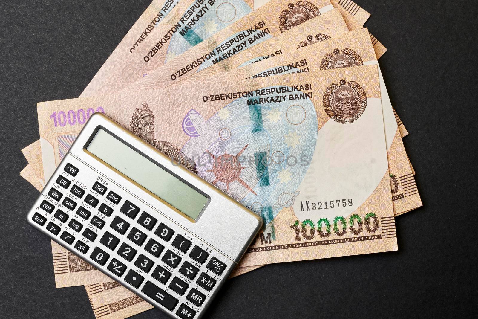 Uzbek money and calculator on black. Pile of Uzbek sums and calculator. Concept of exchange rate. Economic or financial concept
