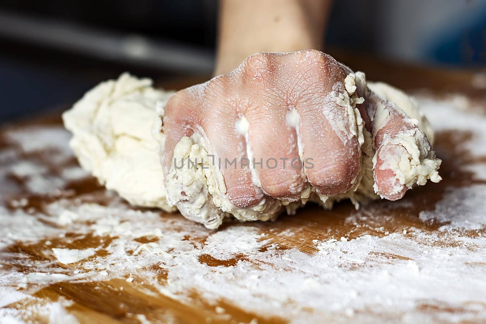 female hand kneading a flour dough by rolling it on a wooden board by rarrarorro
